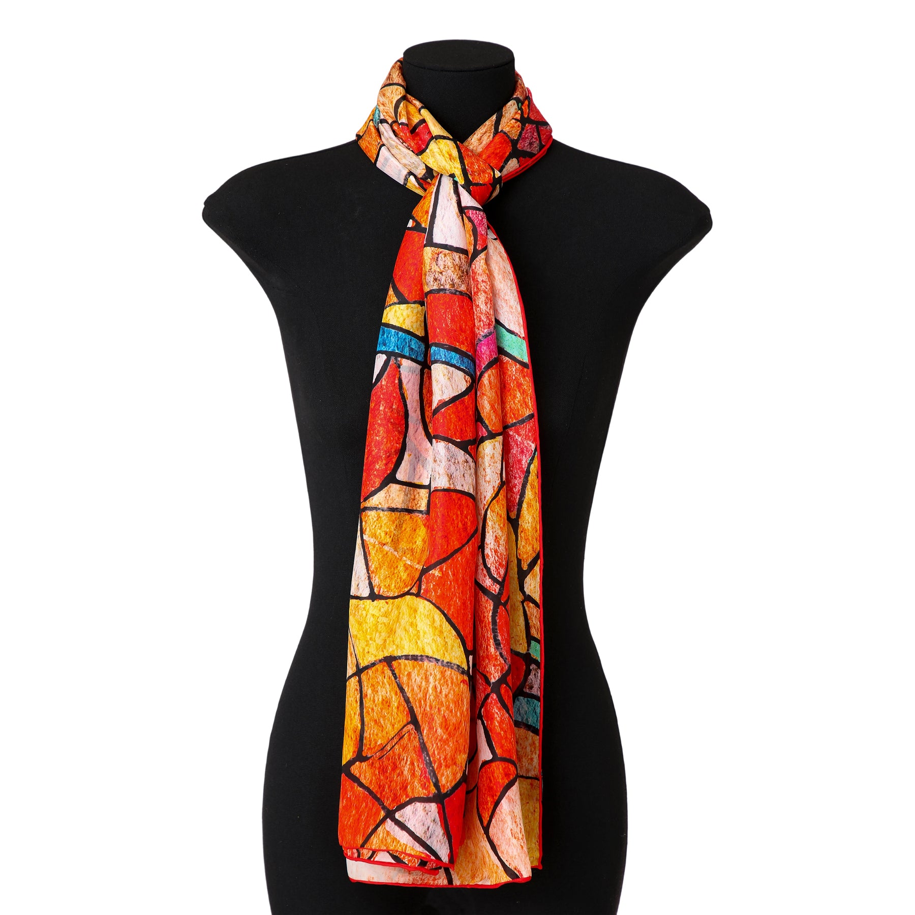 The mannequin showcases the Artistic Silk Scarf Vitrales de Luz, featuring an abstract stained glass pattern in red, orange, yellow, and blue with black lines, draped loosely around the neck like wearable art.
