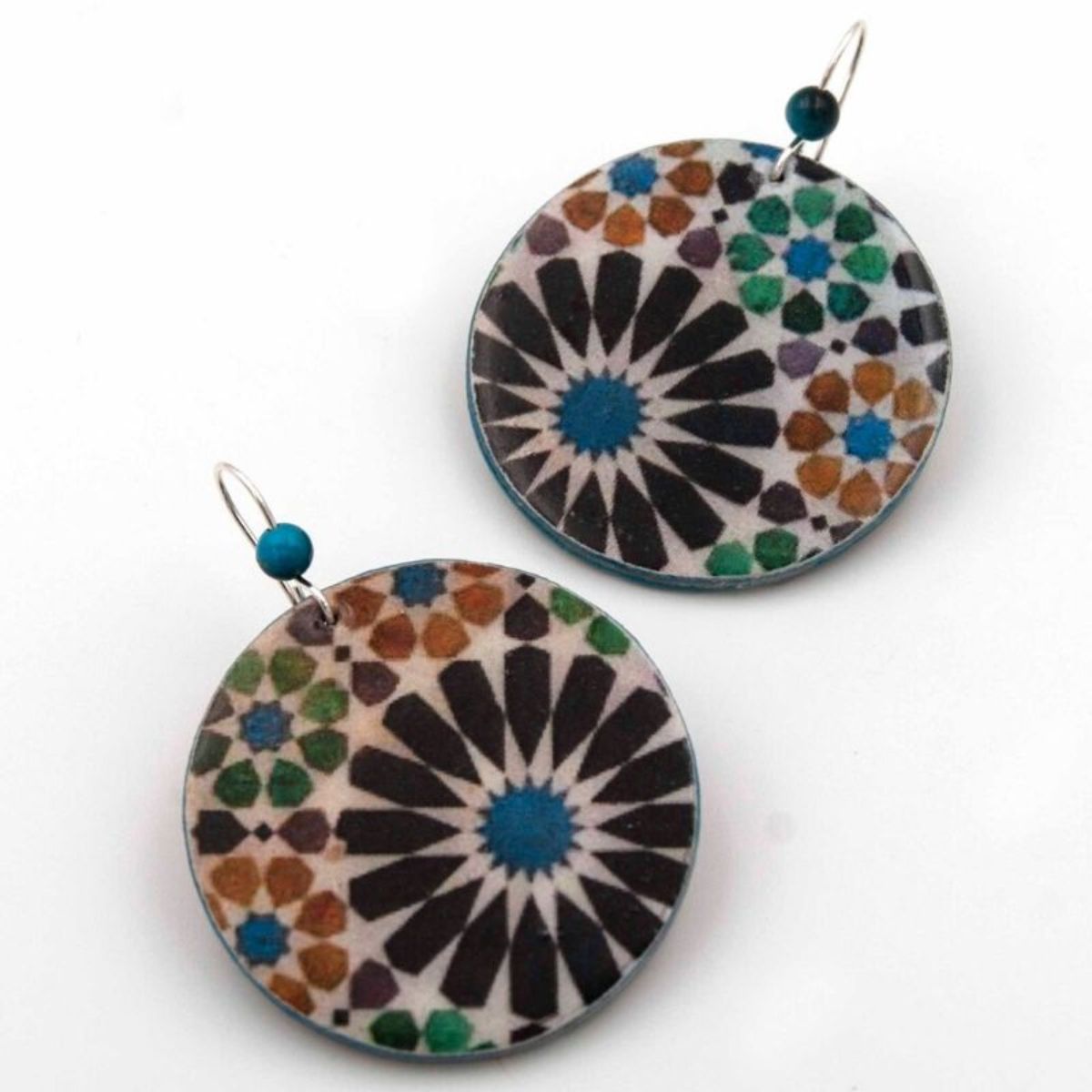 The Big Round Colorful Earrings Benameji by Azul Añil feature a geometric mosaic design in black, brown, turquoise, green, and purple inspired by Islamic art. Made from recycled paper with a central black motif and vibrant shapes, they have silver hooks adorned with a small blue bead.