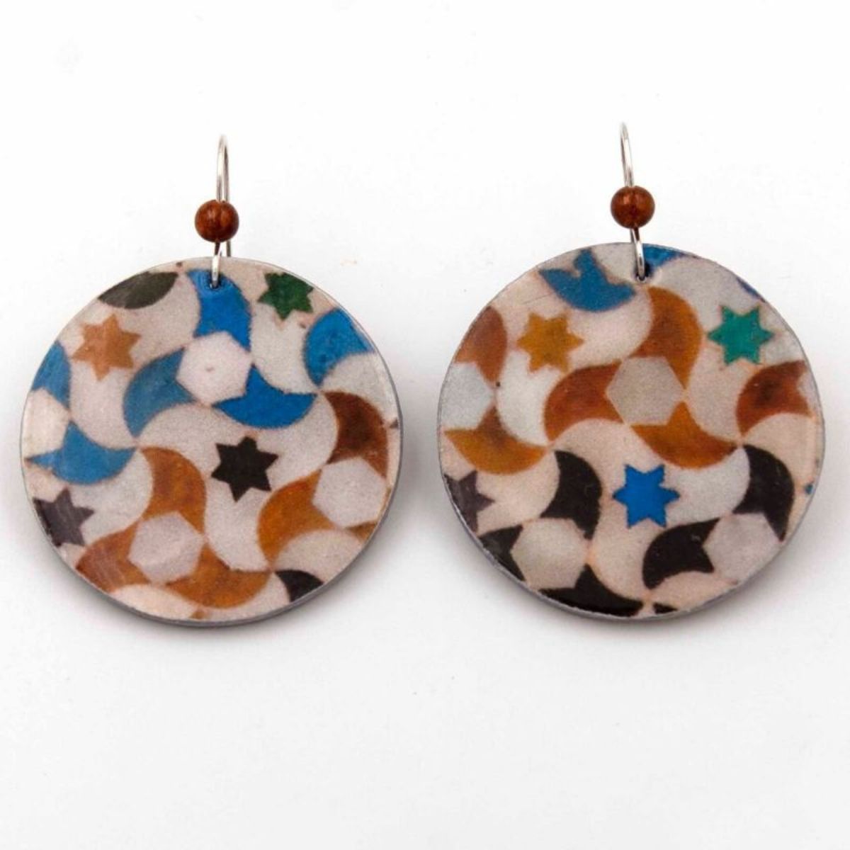 The Round Colorful Earrings Trevélez by Azul Añil feature an oriental Islamic tile-inspired geometric pattern with stars and crescents in blue, brown, black, and white. They are topped with a small brown bead and attached to silver hooks.