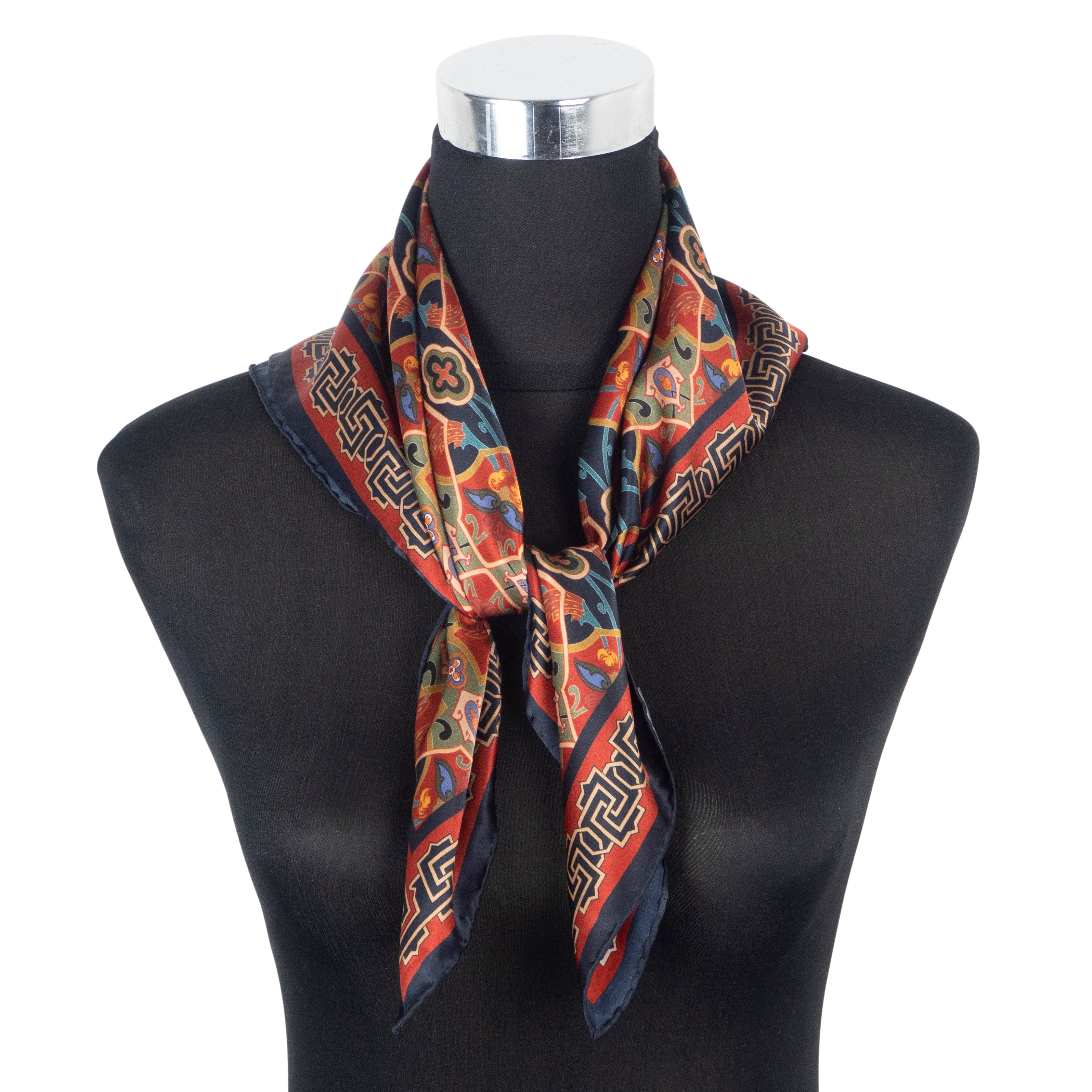 A mannequin displays the Silk Square Neck Scarf Rania, a vibrant square silk scarf with hand rolled hems, decorated with geometric and floral designs inspired by Islamic art in rich red, blue, gold, and green.
