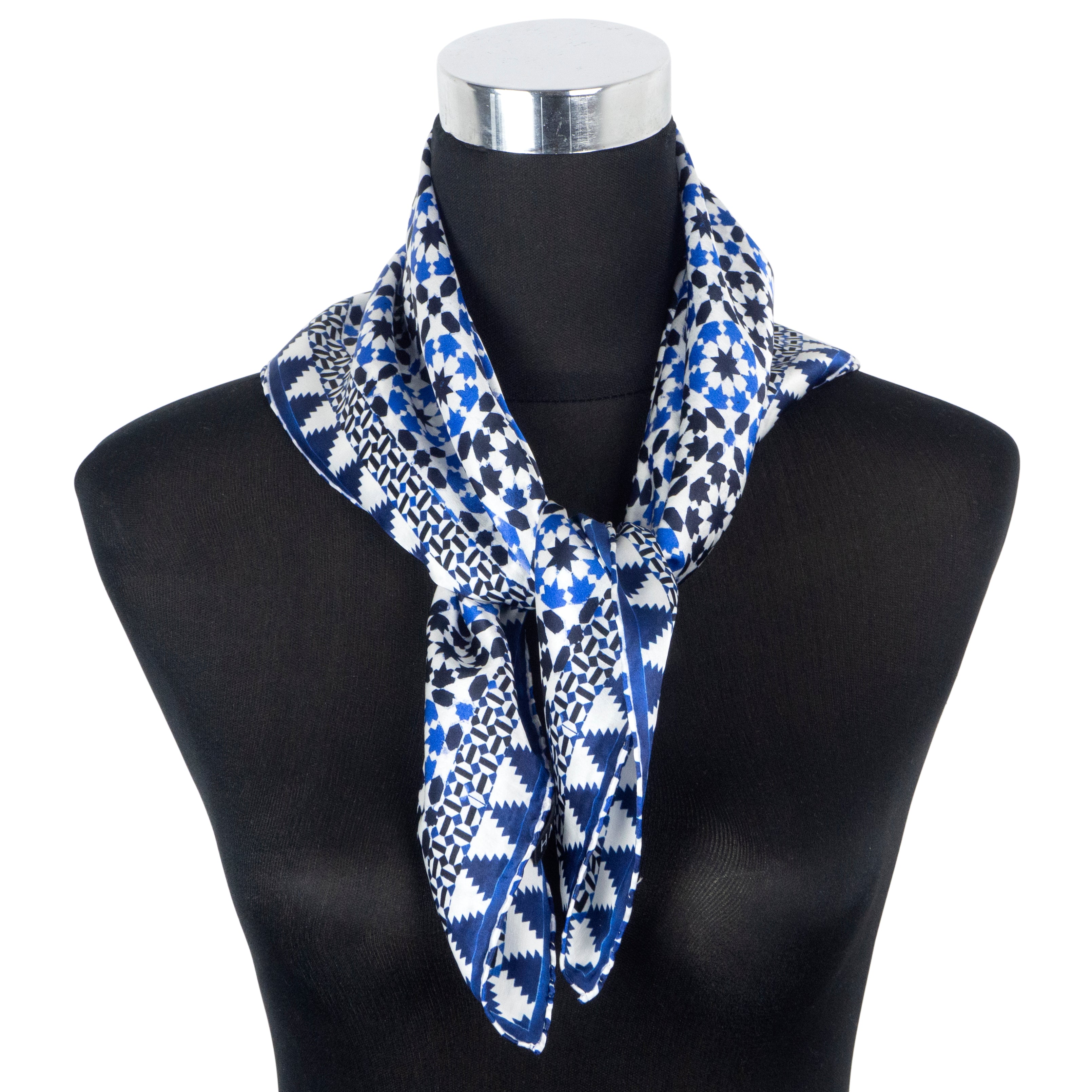 A mannequin displays the Blue Silk Square Scarf Sabika with blue and black geometric patterns, tied loosely around the neck. This scarf features a delicate hand-rolled hem and drapes elegantly down the front.