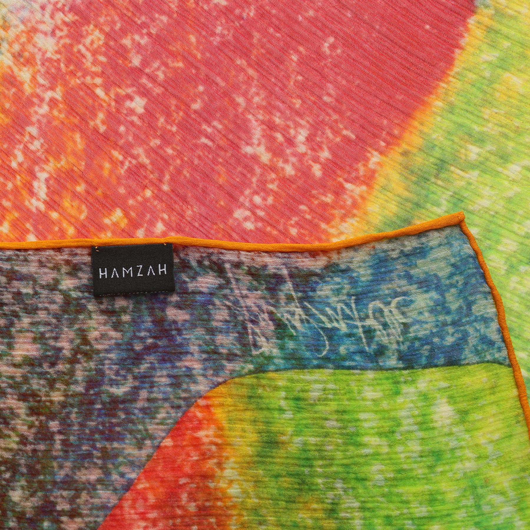 A close-up of the Multicolor Silk Scarf Calidoscopic showcases vibrant red, orange, green, and yellow hues.