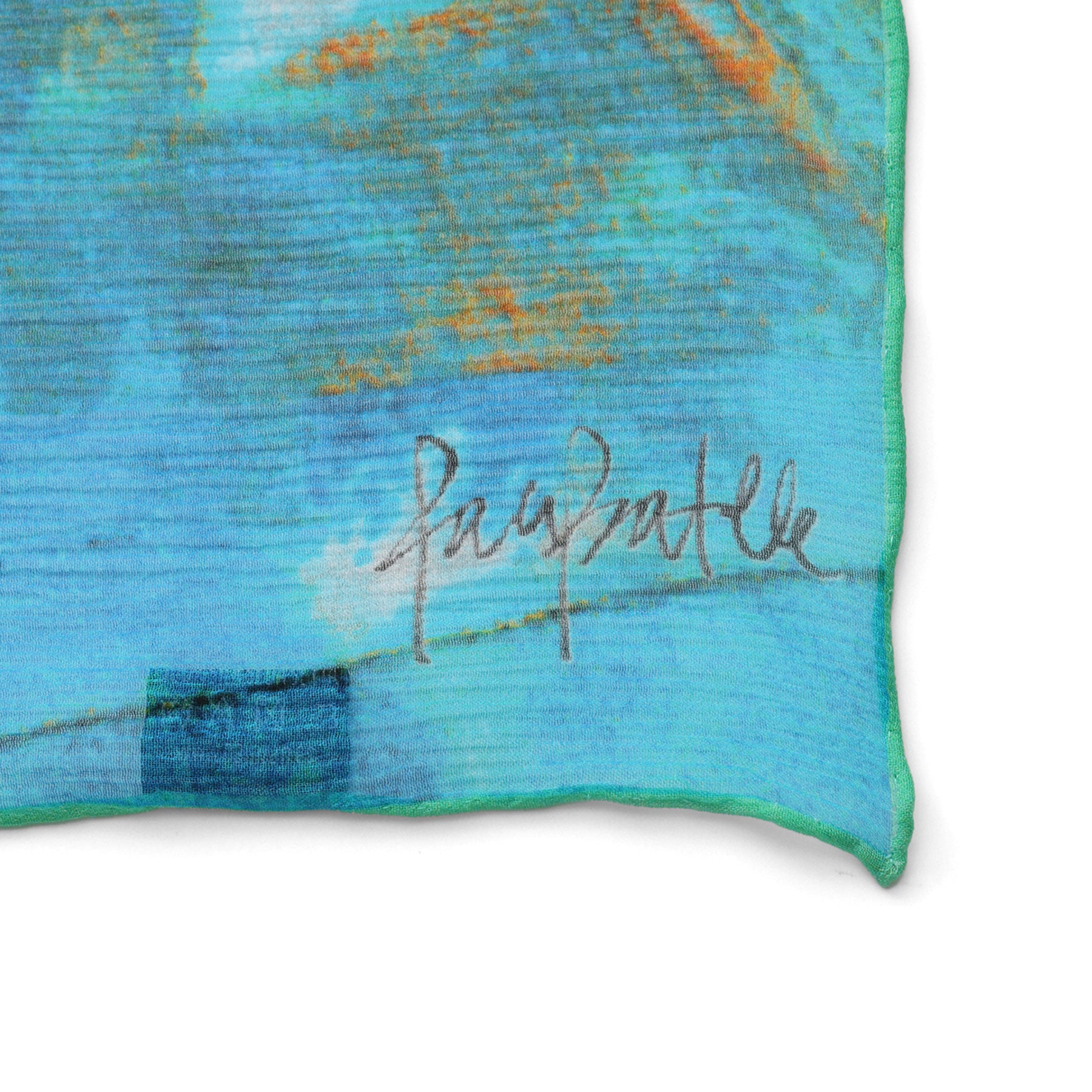 A close-up of the Multicolor Silk Scarf Oxido Marino, showcasing blue and turquoise muslin silk with abstract orange and white patterns and a subtle handwritten signature—wearable artwork in vibrant hues.