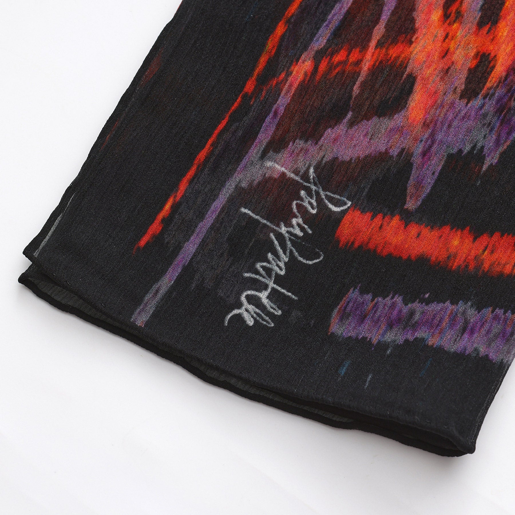 A close-up of the Black & Red Silk Scarf Anubis, featuring black muslin silk with red, orange, and purple abstract designs plus a white handwritten-style signature—an elegant piece of wearable art against a white background.