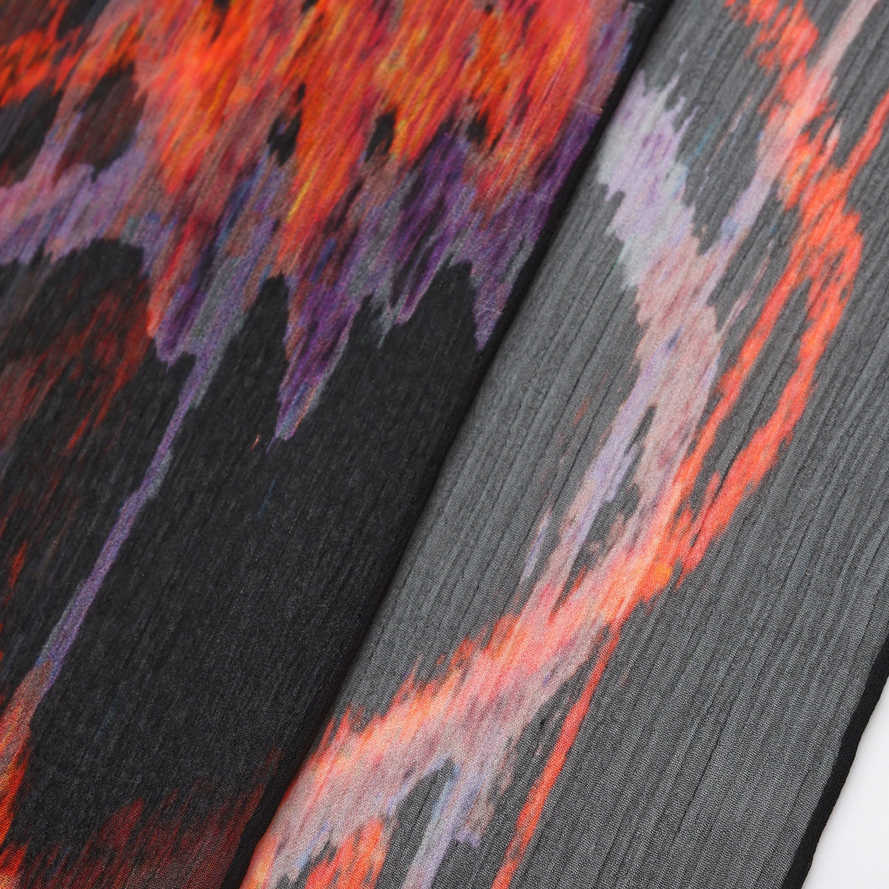 Close-up of the Black & Red Silk Scarf Anubis, featuring colorful, abstract patterns in red, orange, purple, and black with vibrant jagged designs and diagonal lines—a bold piece of Mediterranean-inspired wearable art.