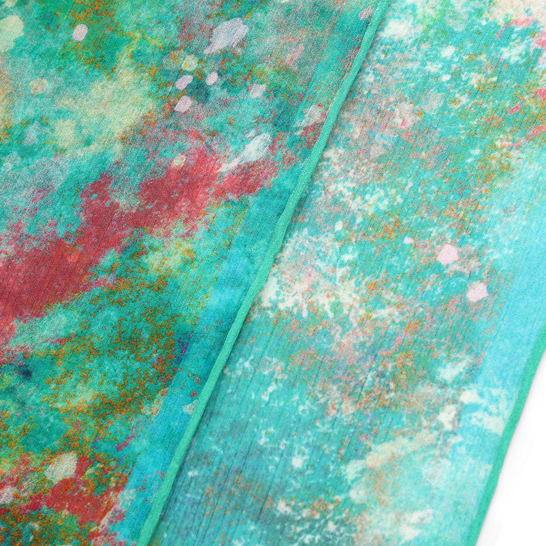 A close-up of the Natural Silk Scarf Mundos Ocultos reveals vibrant teal, turquoise, red, orange, and white abstract patterns, highlighting its colorful look and artisanal craftsmanship.