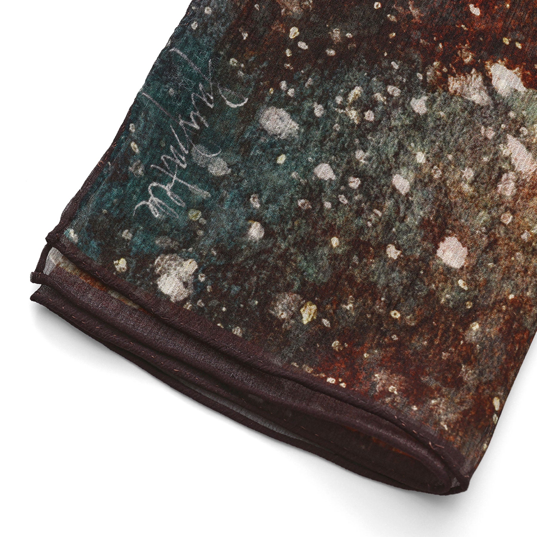 A close-up of the Multicolor Silk Scarf Polvo Cósmico shows its abstract splotches of teal, brown, and cream on muslin silk with a subtle cursive signature—truly wearable artwork.