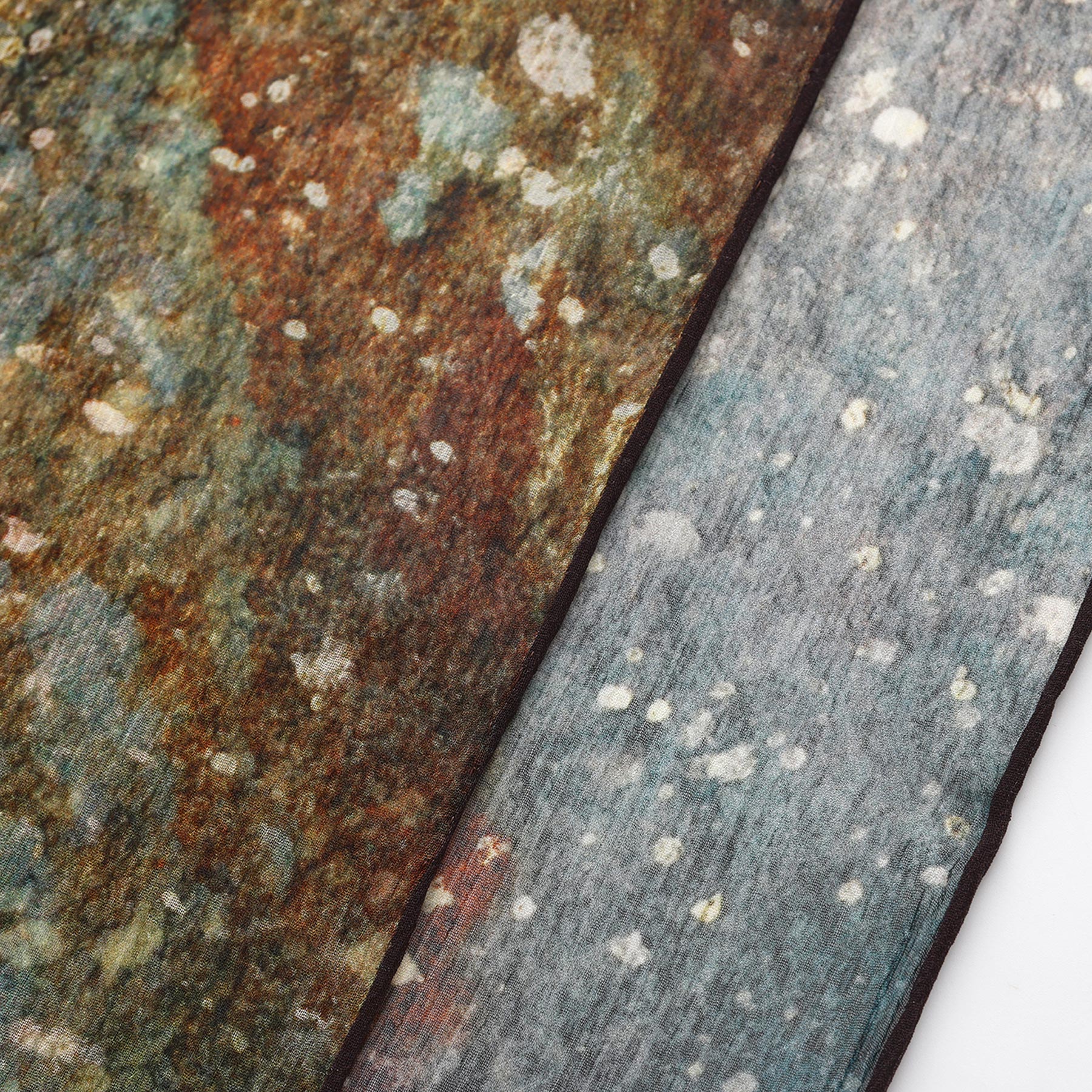 Close-up of the Multicolor Silk Scarf Polvo Cósmico: semi-transparent muslin silk in rusty brown, green, and bluish-grey tones with mottled patterns and white spots, creating a unique piece of wearable art.