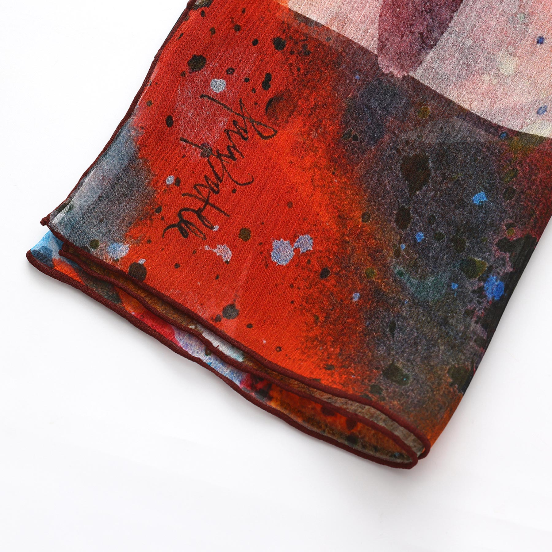 A close-up of the Multicolor Silk Scarf Cangrejos: Mediterranean silk adorned with abstract red, black, blue, and white splashes, plus stylized black writing in one corner—an elegant piece of wearable art.