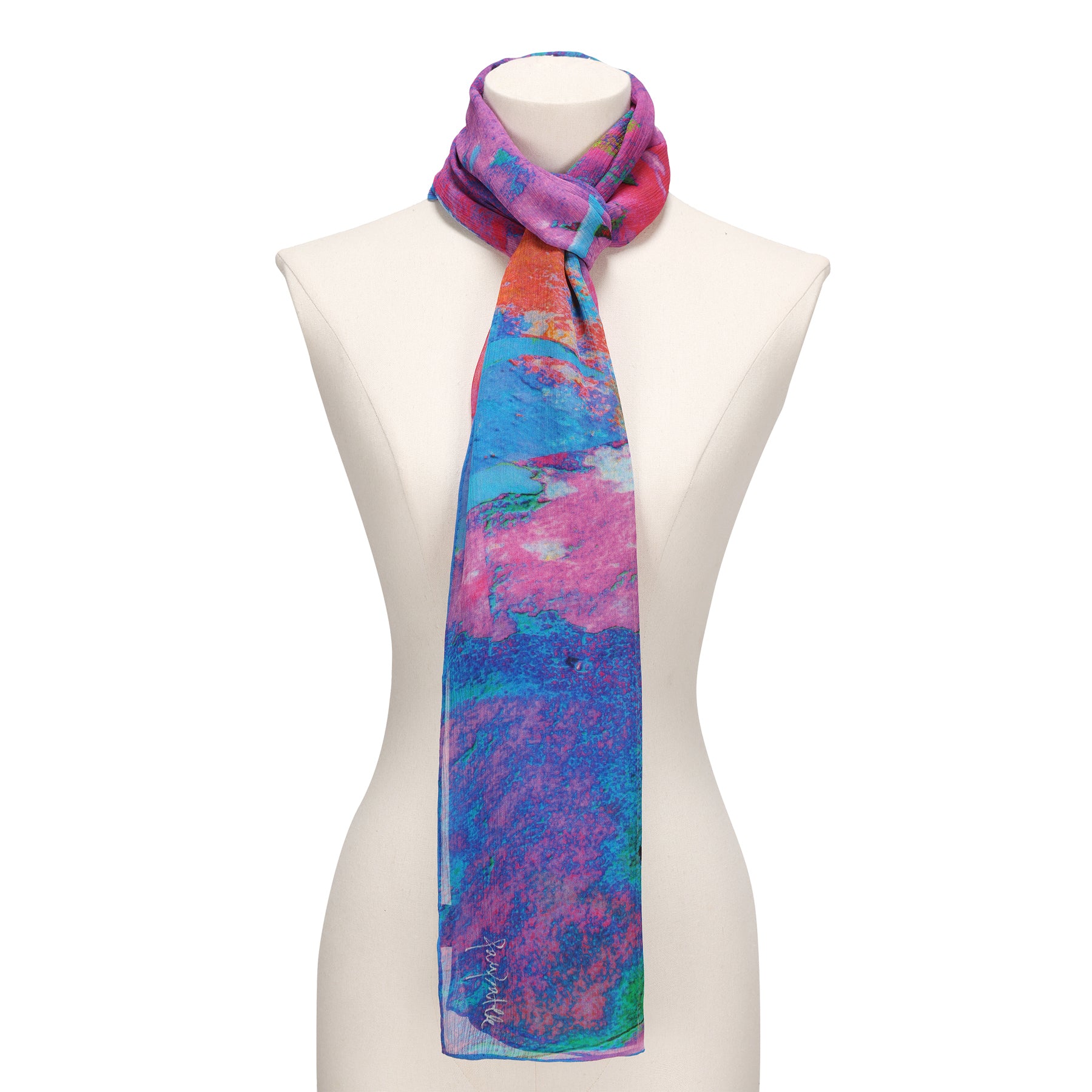 The Multicolor Silk Scarf Océano Fucsia, featuring blue, pink, orange, and purple abstract patterns in muslin silk, drapes elegantly around a white mannequin’s neck—a striking piece of wearable art.