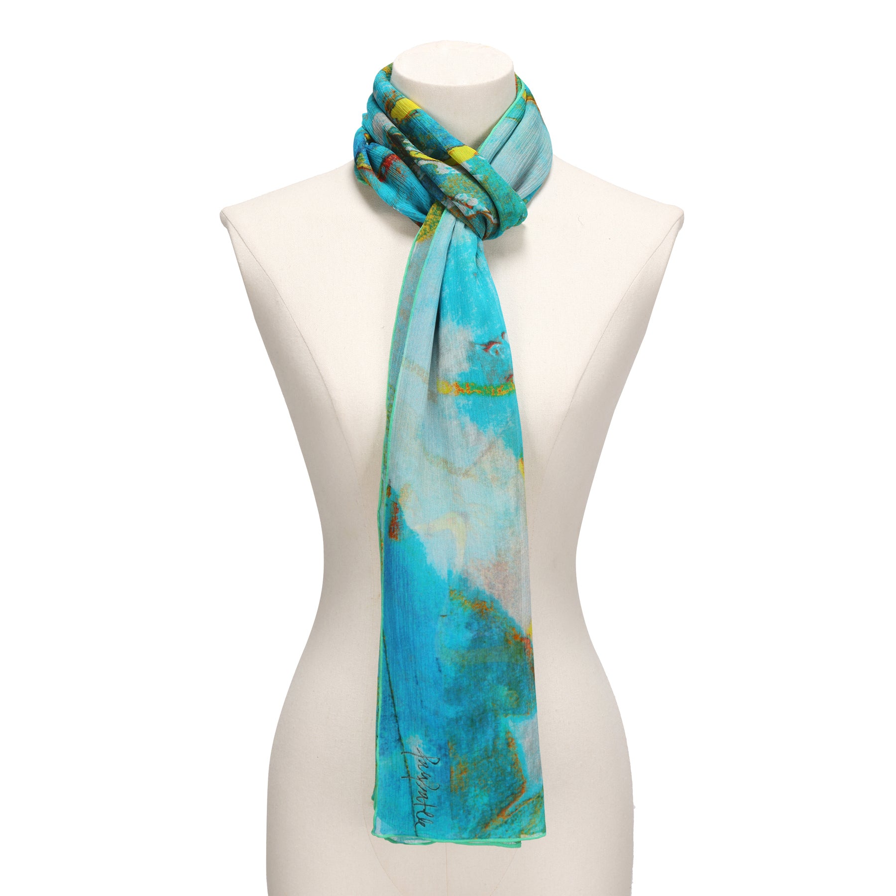 A mannequin showcases the Multicolor Silk Scarf Oxido Marino, featuring bright blue, teal, and yellow watercolor patterns draped loosely around the neck—a true piece of wearable art.