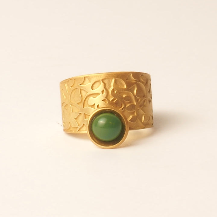 The Platónica Ring Inspired by Nasrid Motifs Gold & Green features a wide gold band with engraved floral patterns and a central round green gemstone in a gold bezel, drawing inspiration from the Alhambra monument.