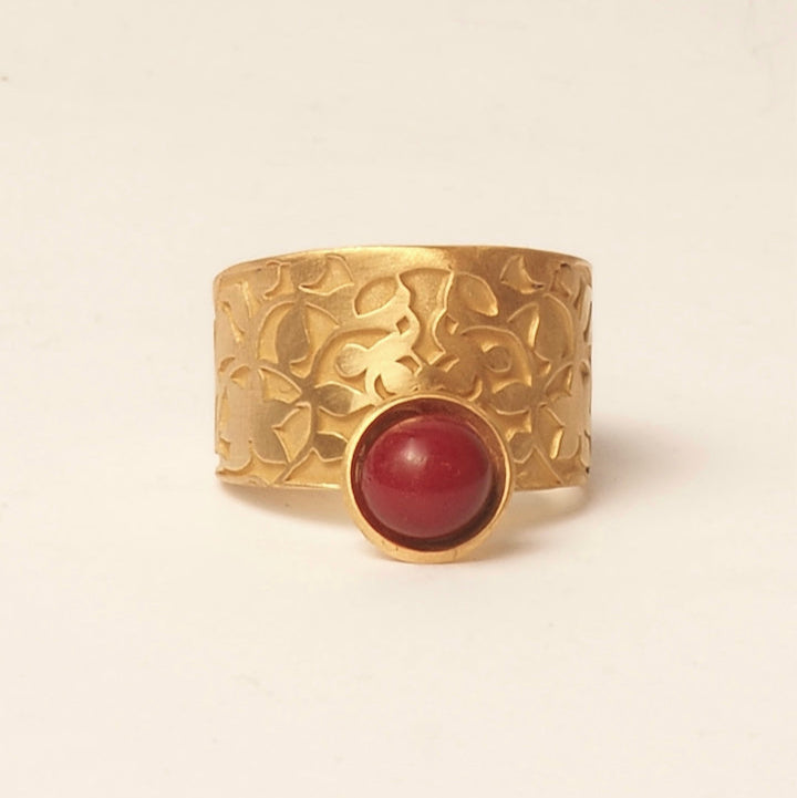 The Nasrid Palaces Detail Ring Red Gold by Platónica is a wide gold ring with intricate floral engravings featuring a prominent round red stone in the center, set against a plain white background.