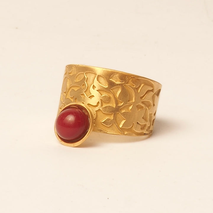 The Platónica Nasrid Palaces Detail Ring in red gold features intricate floral engravings and a prominent, rounded red stone set in a bezel on one side, reflecting the elegance of the Alhambra collection against a plain, light background.