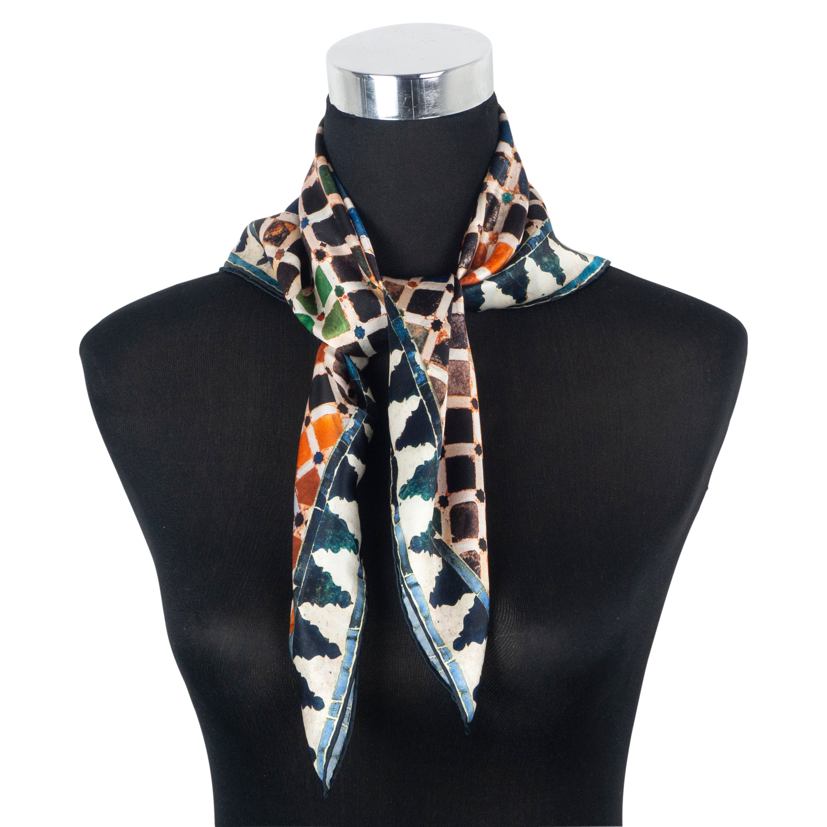 The Multicolor Silk Square Scarf Comares, crafted from pure silk with hand rolled hems, showcases geometric shapes in brown, green, orange, and blue and is tied around the neck of a black mannequin bust with a silver cap.
