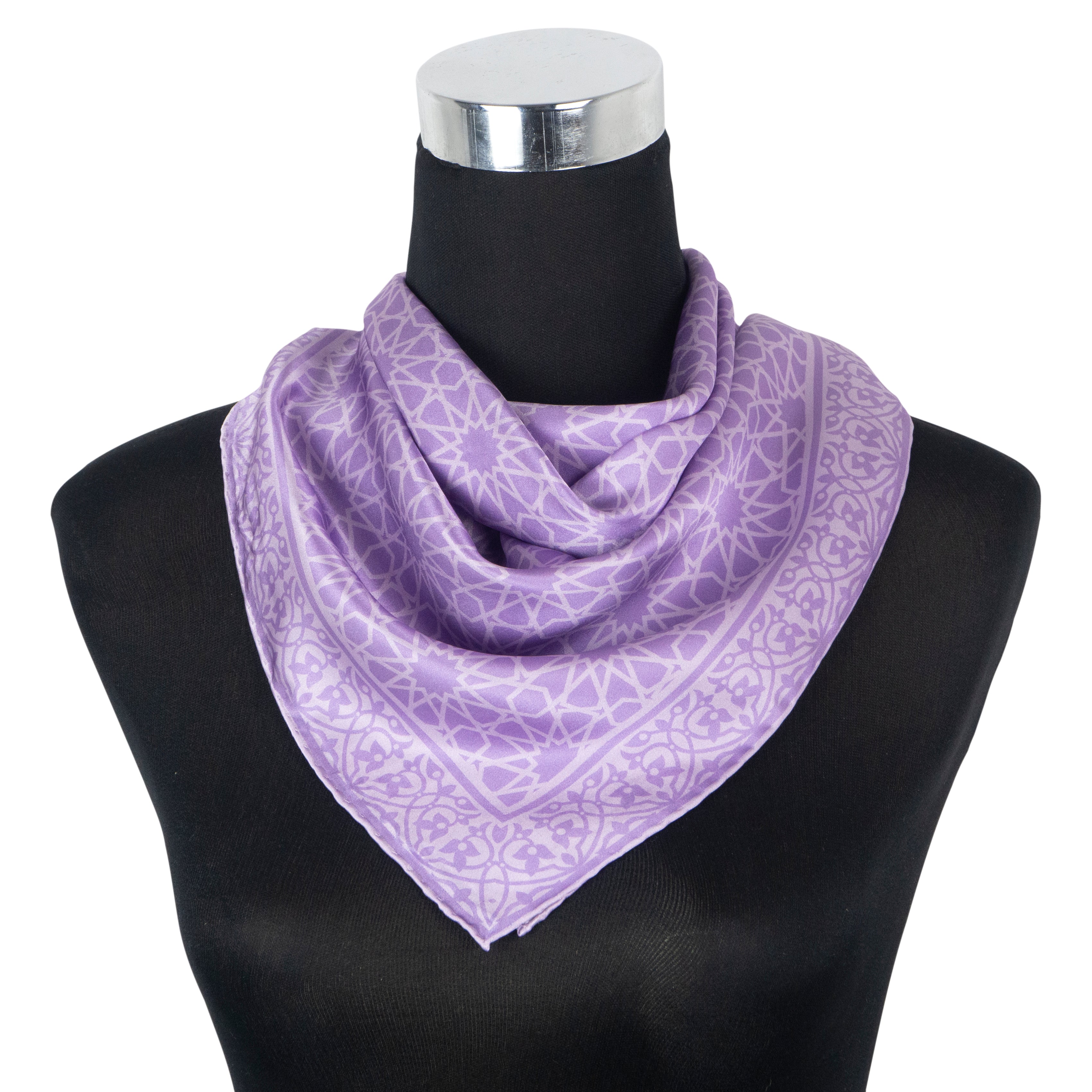 A black mannequin showcases the Purple Silk Square Scarf Dalila, featuring a silky purple fabric with geometric patterns and hand-rolled hems, draped loosely around the neck in a triangular style.
