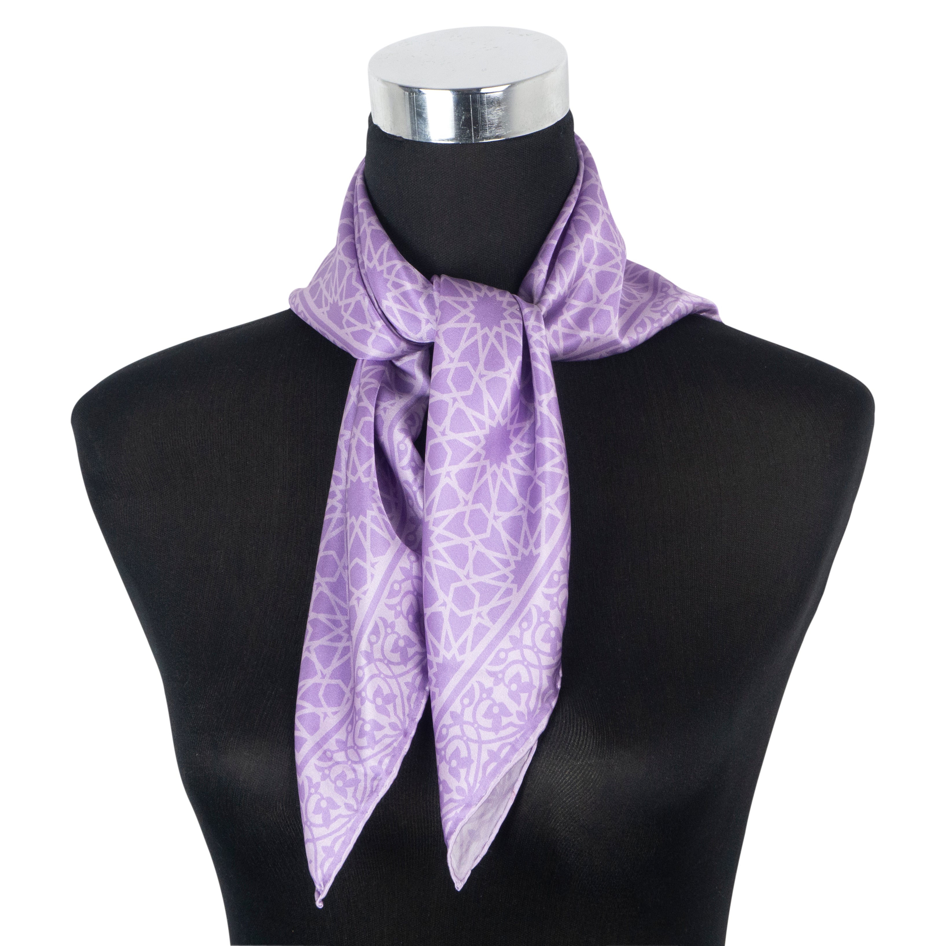 A black mannequin displays the Dalila Purple Silk Square Scarf, featuring a geometric pattern and luxurious finish, tied stylishly around the neck.