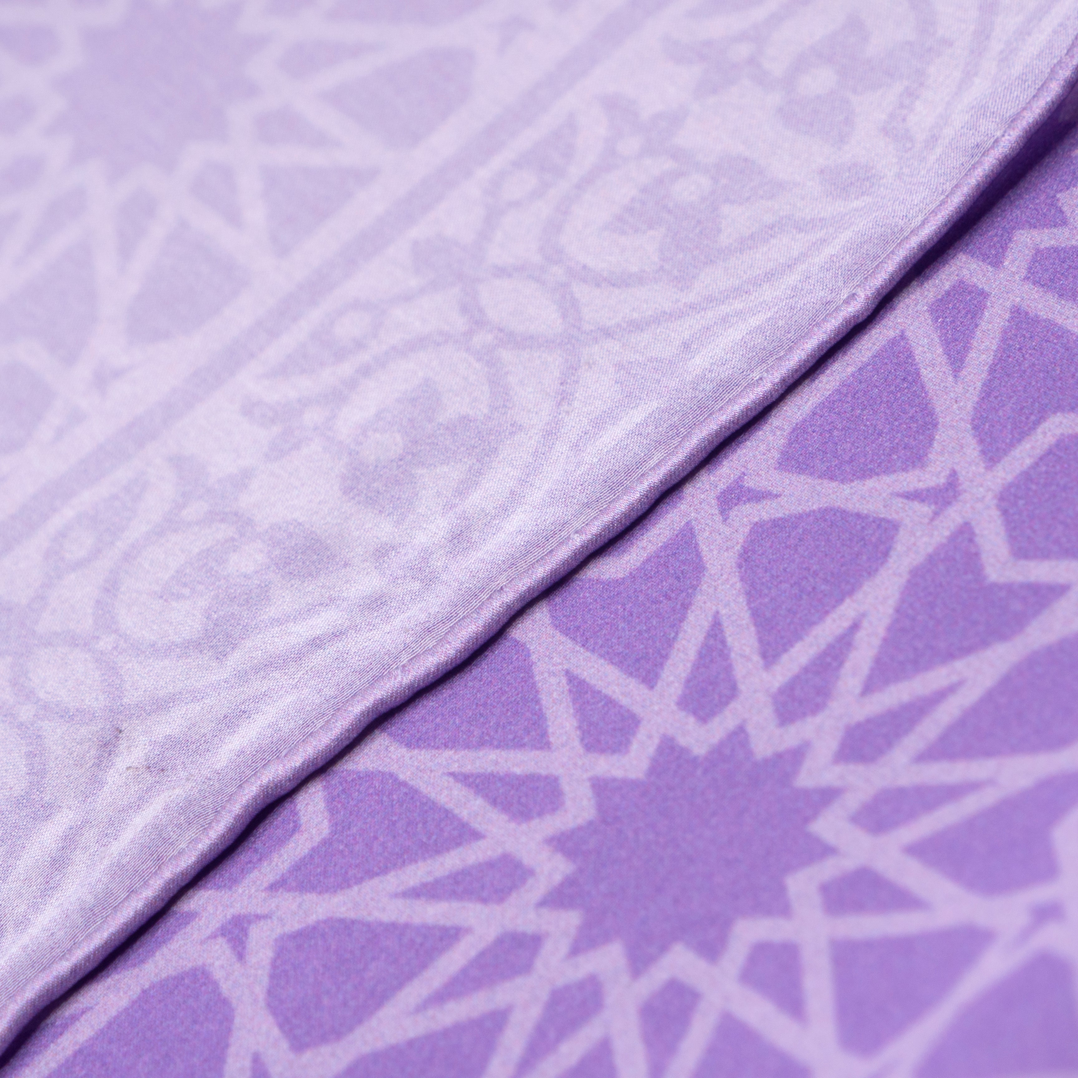 Close-up of the Purple Silk Square Scarf Dalila, featuring two overlapping luxurious purple fabrics with geometric star patterns and intricate designs, creating a visually appealing layered effect.