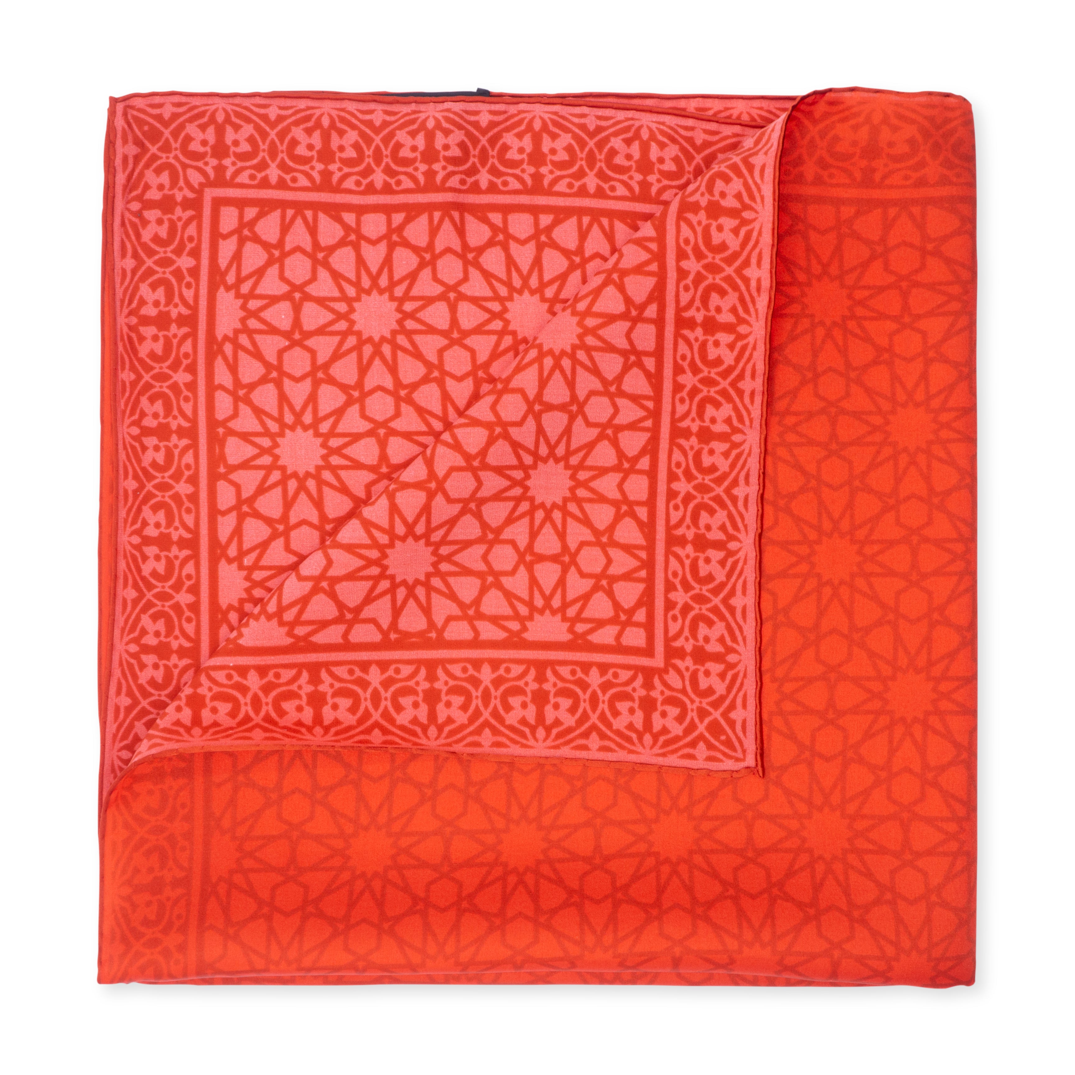 The Red Silk Square Scarf Dalila, handcrafted in Turkey, features an intricate lighter red geometric pattern and is neatly folded with a corner turned over to display its exquisite design on both sides.