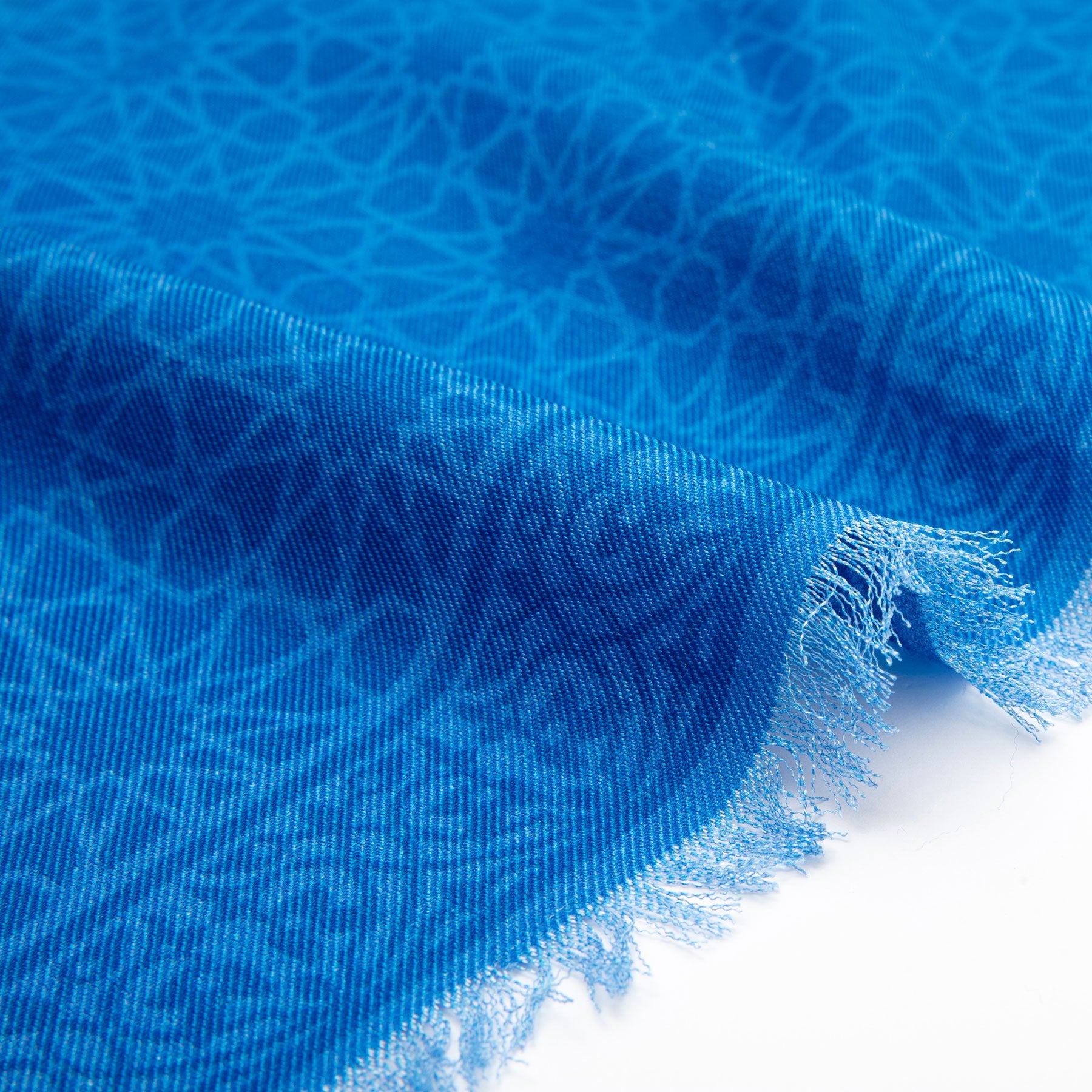 A close-up of the Silk and Wool Blue Scarf Dalila, featuring a subtle geometric pattern and frayed edges, displayed against a white background.