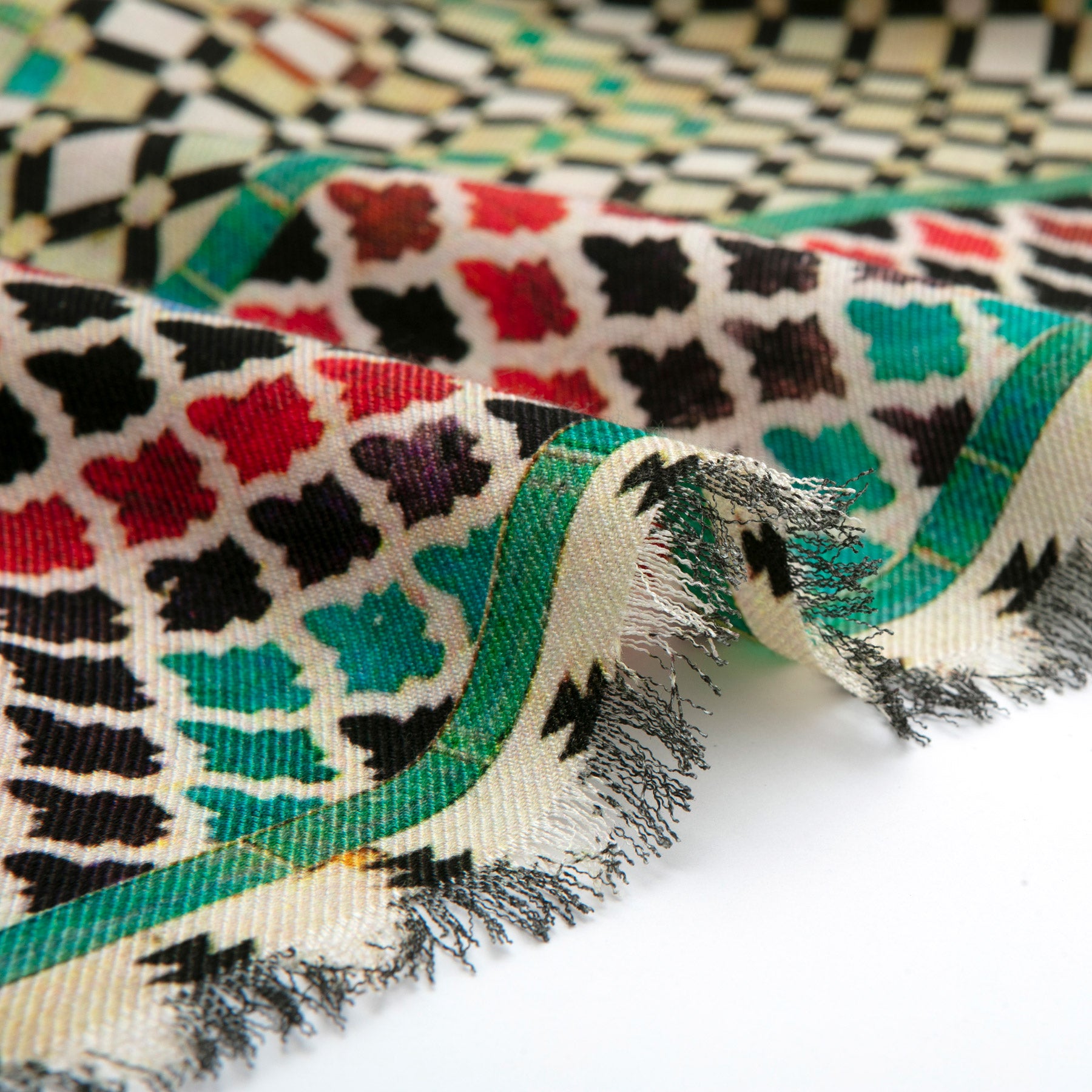 A close-up of Silk and Wool Scarf Hub, displaying textured fabric with fringe edges, featuring Islamic art-inspired geometric and floral patterns in red, black, green, and brown, bordered by green and cream lines.