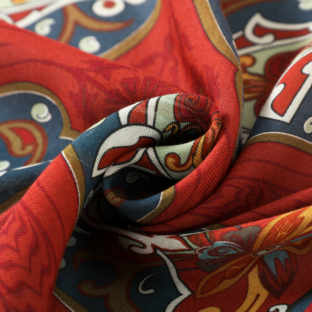 A close-up of the Isfahan-Inspired Red & Blue Scarf – 100% Modal, twisted into a swirl, showcasing its vibrant red, blue, yellow, and white floral and geometric patterns inspired by traditional art.