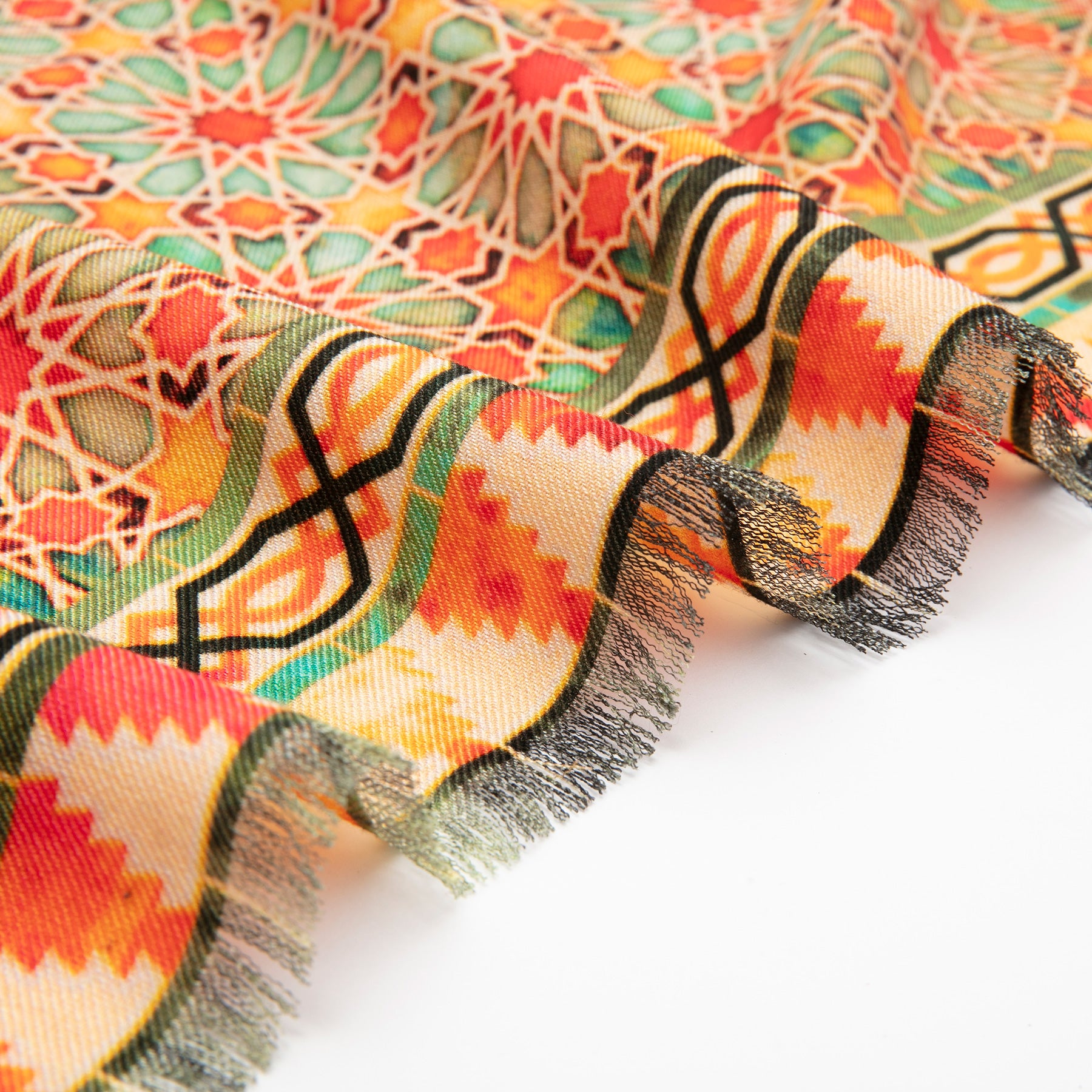 The Wool & Silk Islamic Art Inspired Orange Scarf features intricate geometric and floral patterns in vibrant orange, red, green, and yellow, with a fringed edge adding texture as it rests folded on a white surface.