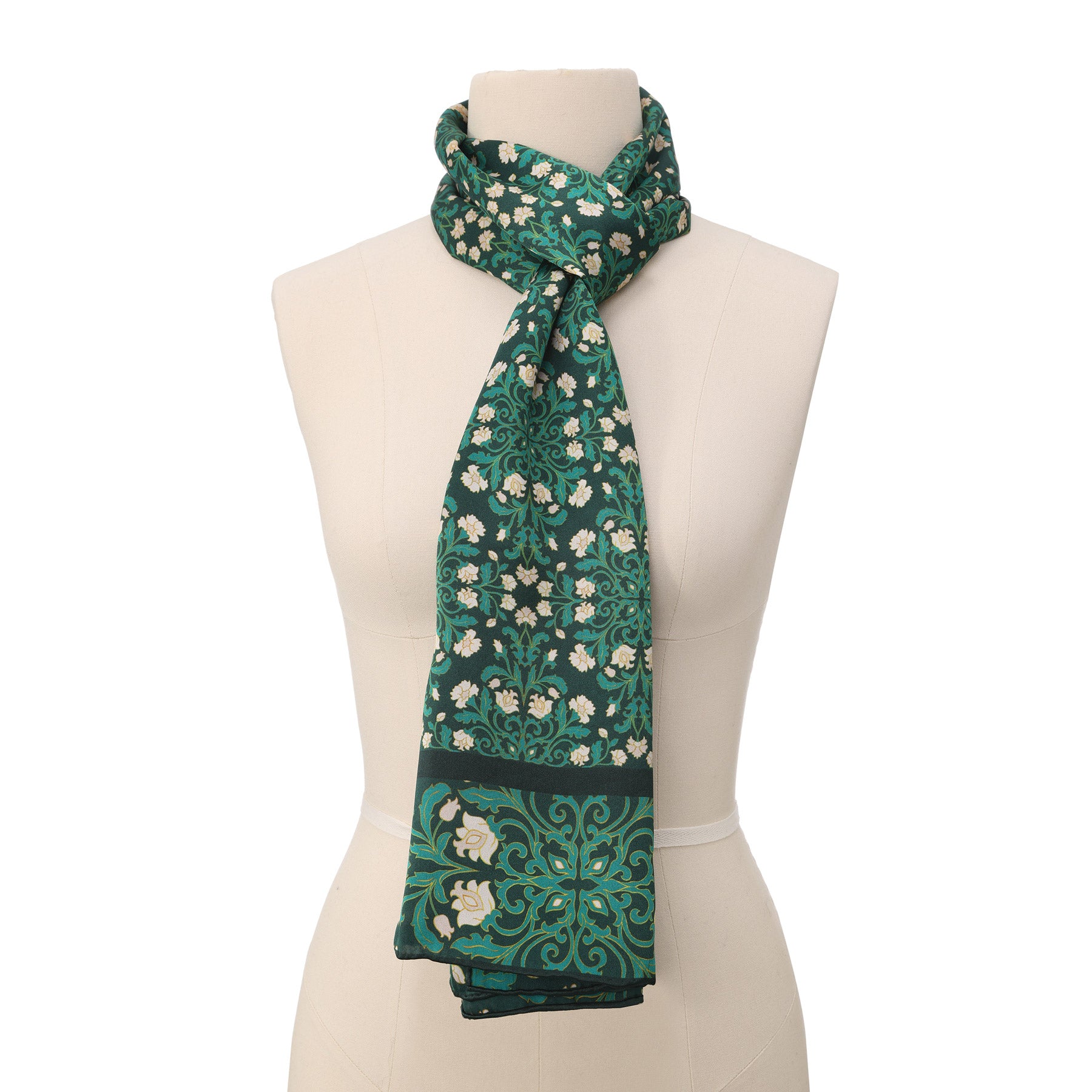 A close-up of the Floral Green Silk Scarf with Delicate White Blooms, draped to highlight its soft silk texture and intricate white floral pattern with swirling leaves in an art nouveau style.