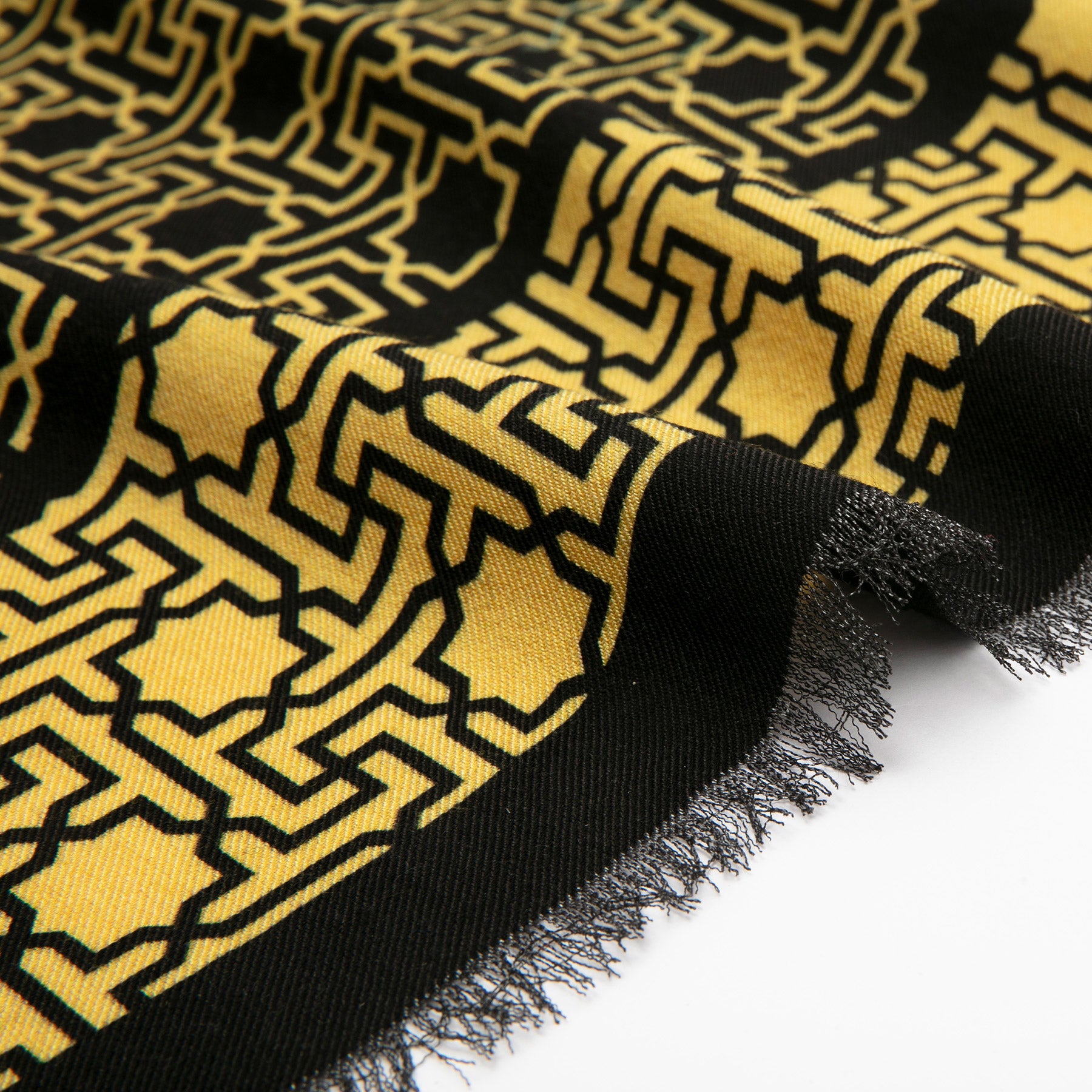 A close-up of the Silk Wool Black and Gold Scarf Rawdah V3, featuring bold black geometric Islamic-inspired designs and fringed edges in a yellow-gold hue, displayed on a white surface.