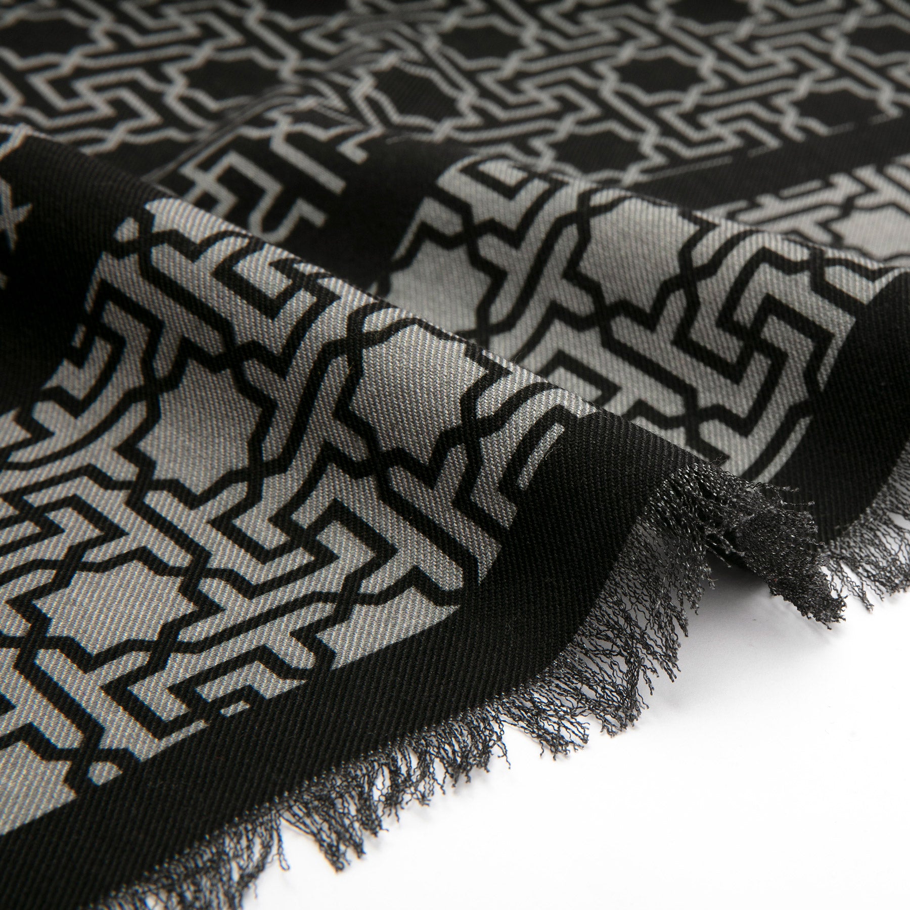 Close-up of the Silk Wool Black and Gray Scarf Rawdah V1 highlights its textured fabric, frayed edges, and intricate Islamic geometry-inspired print in black and gray, with gentle folds that enhance its distinctive appeal.