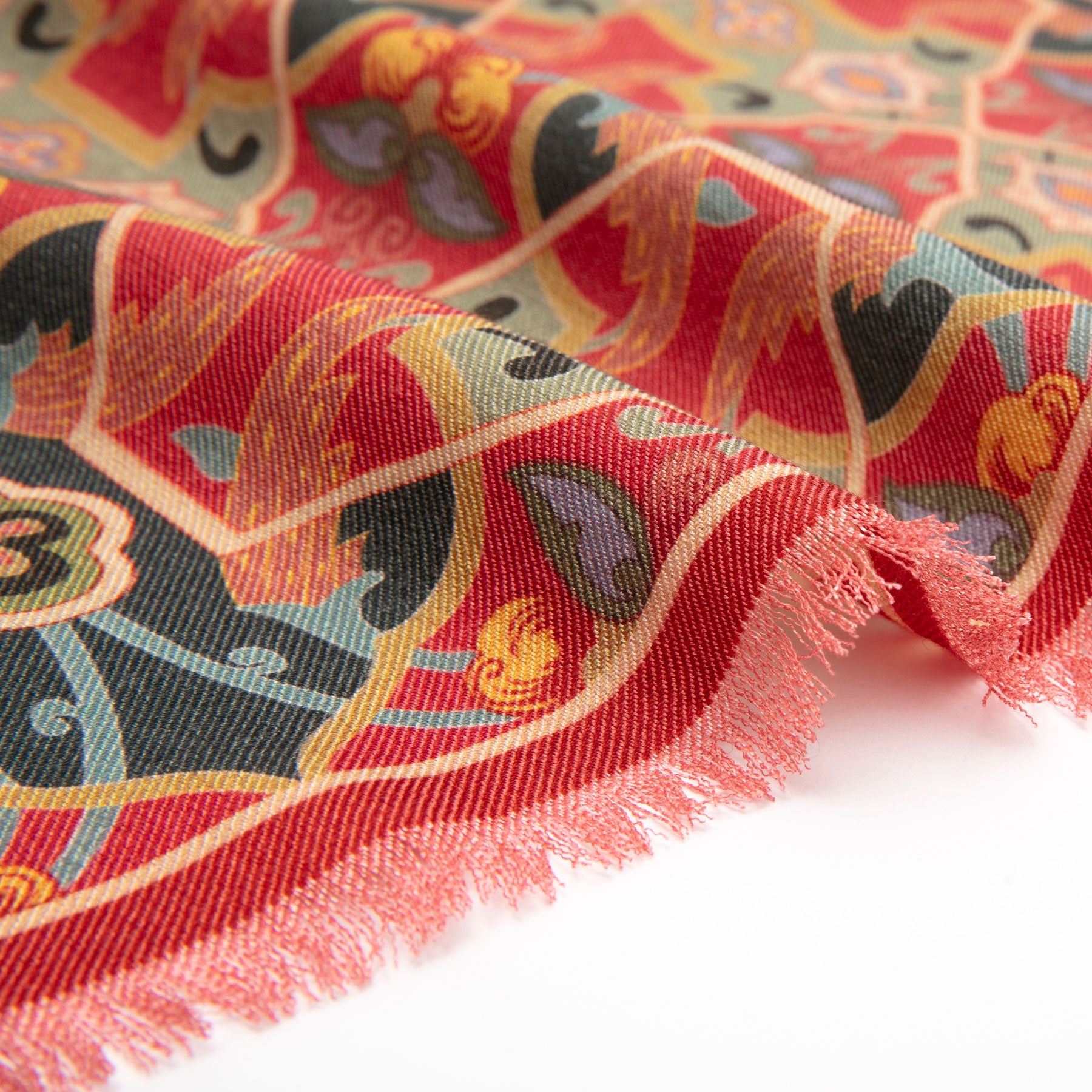 A close-up of the Silk and Wool Red Scarf Rania, featuring gold, black, and green ornate designs inspired by Islamic art prints, with a fringe along the edge, set against a white background.