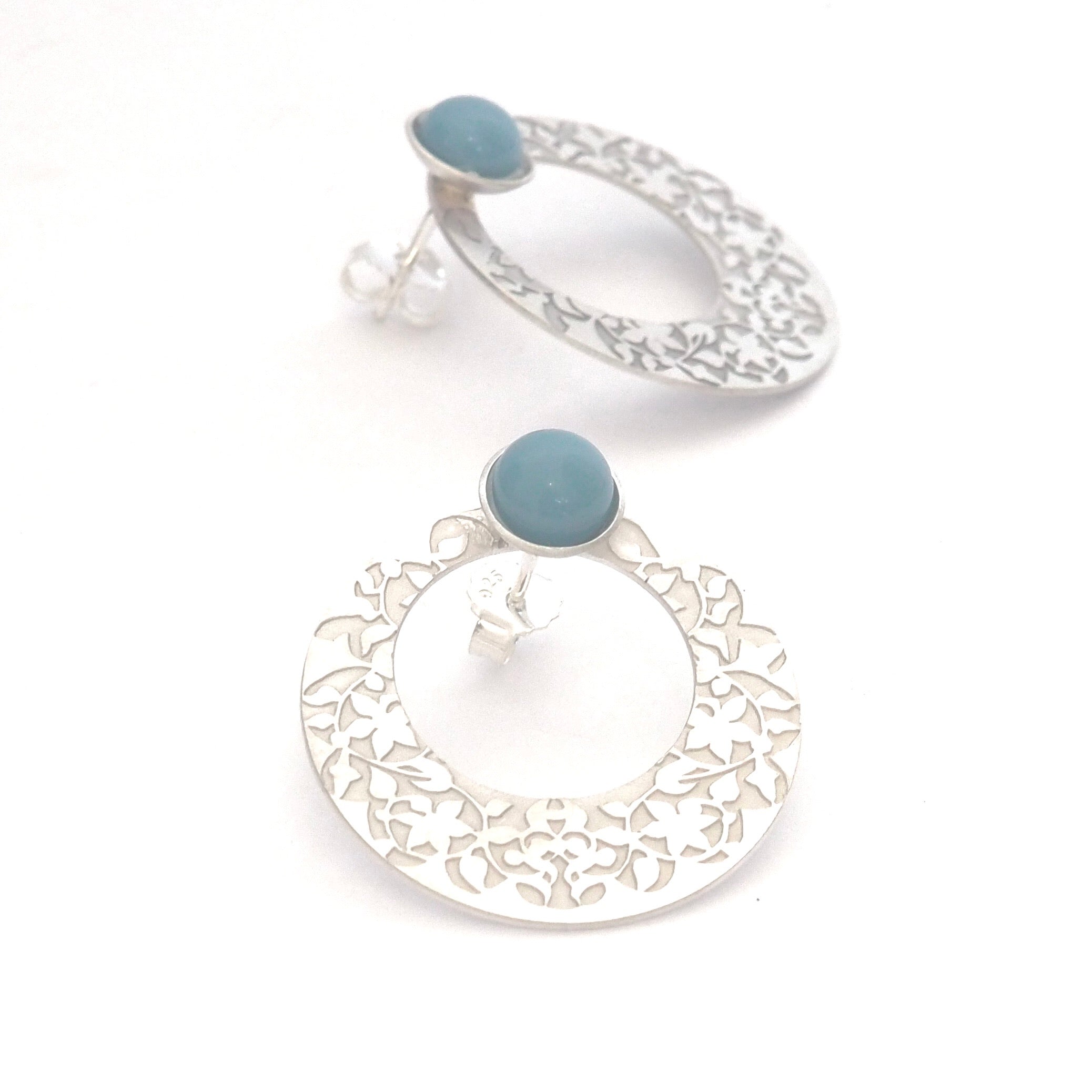 Presenting the Blue Nasrid Palaces Detail Earrings by Platónica: two exquisite 925 silver earrings from the Alhambra collection, adorned with intricate floral cut-out designs and topped with a blue stone. One earring stands upright while the other is laid flat, showcasing their fine craftsmanship.