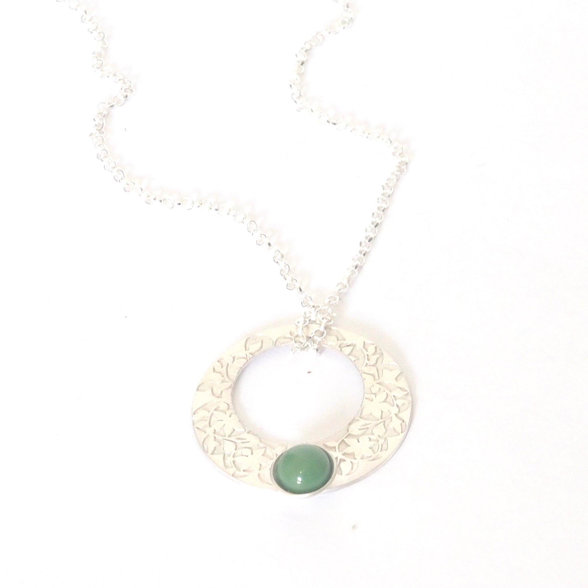 From the Platónica brand, the Green Nasrid Palaces Detail Pendant is a silver necklace featuring a circular pendant with intricate floral patterns. Made from 925 silver, it includes a small green gemstone at the bottom and a thin, delicate chain for an elegant touch to any ensemble.