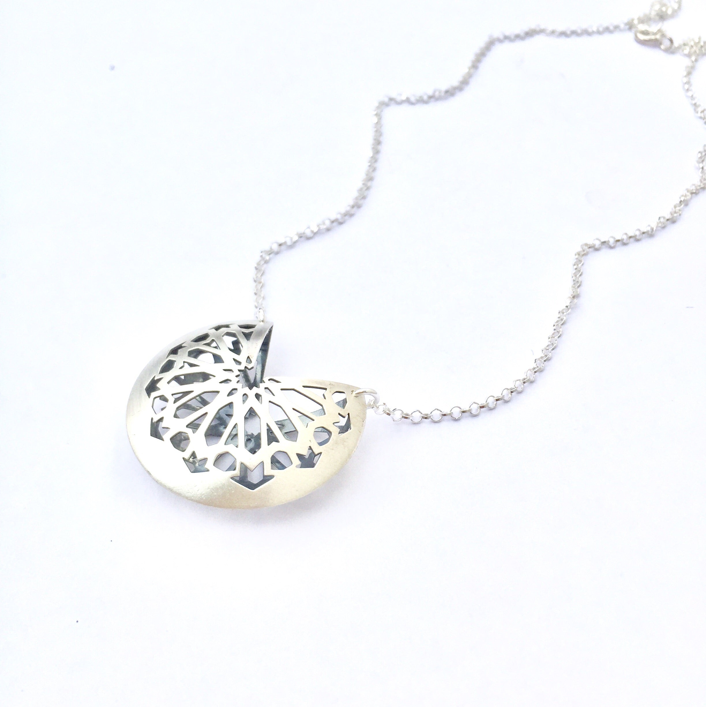 The Platónica Star Pendant Chain is a 925 Silver necklace with a circular pendant featuring an intricate starburst cut-out, showcasing modern jewelry elegance. Its delicate chain reflects the Andalusí collections spirit against a plain white backdrop.