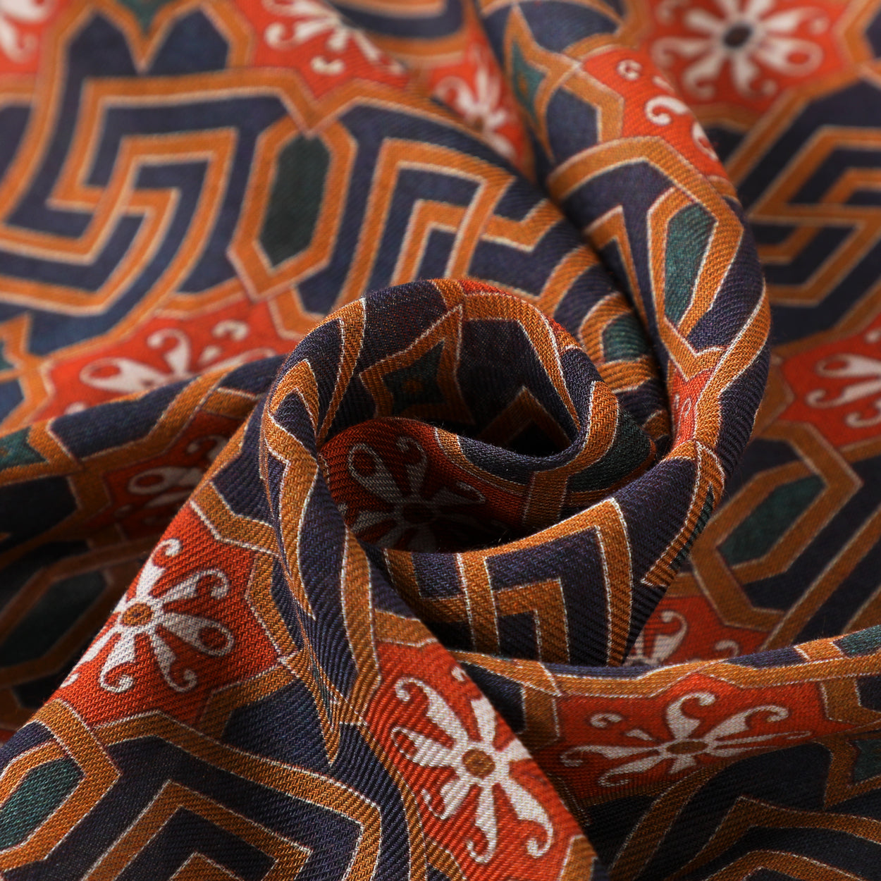 A close-up of the Scarf with Islamic Art-Inspired Geometric Print Lyabi, showing premium modal fabric gathered in a swirl, featuring vibrant orange, navy blue, white, and green geometric and floral patterns.