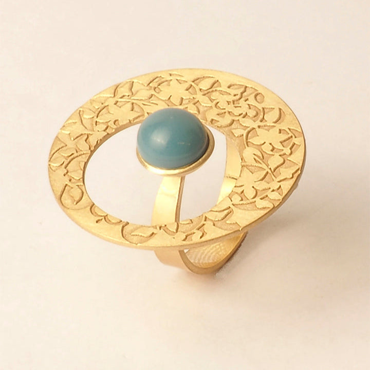The Platónica Alhambra Palace-Inspired Gold Ring for Women features a floral pattern with a prominent blue glass stone in an open circular design, photographed on a plain white background.