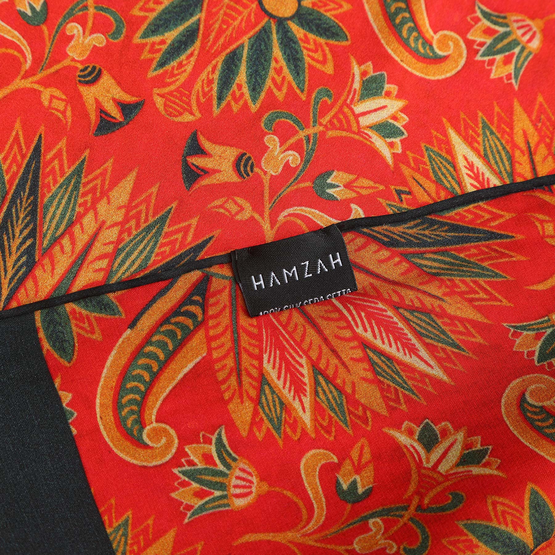 Hamzah-branded packaging with a window displaying the red silk scarf’s bold design, featuring the slogan ‘Wrap yourself in elegance’ beneath.