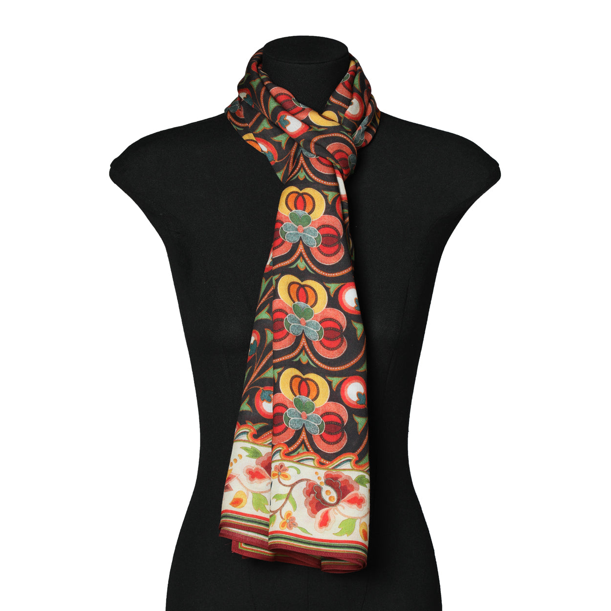 A mannequin showcases the Saroyi Floral Black Scarf – Isfahan Inspired Design, featuring bold red, yellow, green, and blue floral motifs with a decorative Middle Eastern-inspired border and lighter floral accents along the bottom edge.