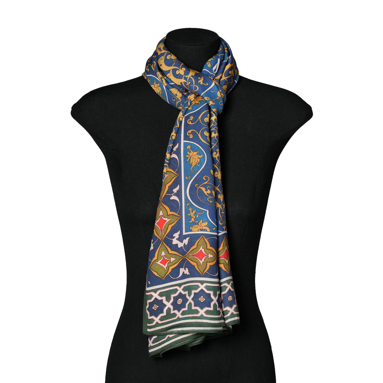 A black mannequin displays the Elegant Blue and Green Scarf with Arabesque Motifs Amiri, made from 100% Modal and featuring intricate gold and red patterns, draped around the neck in a traditional style.