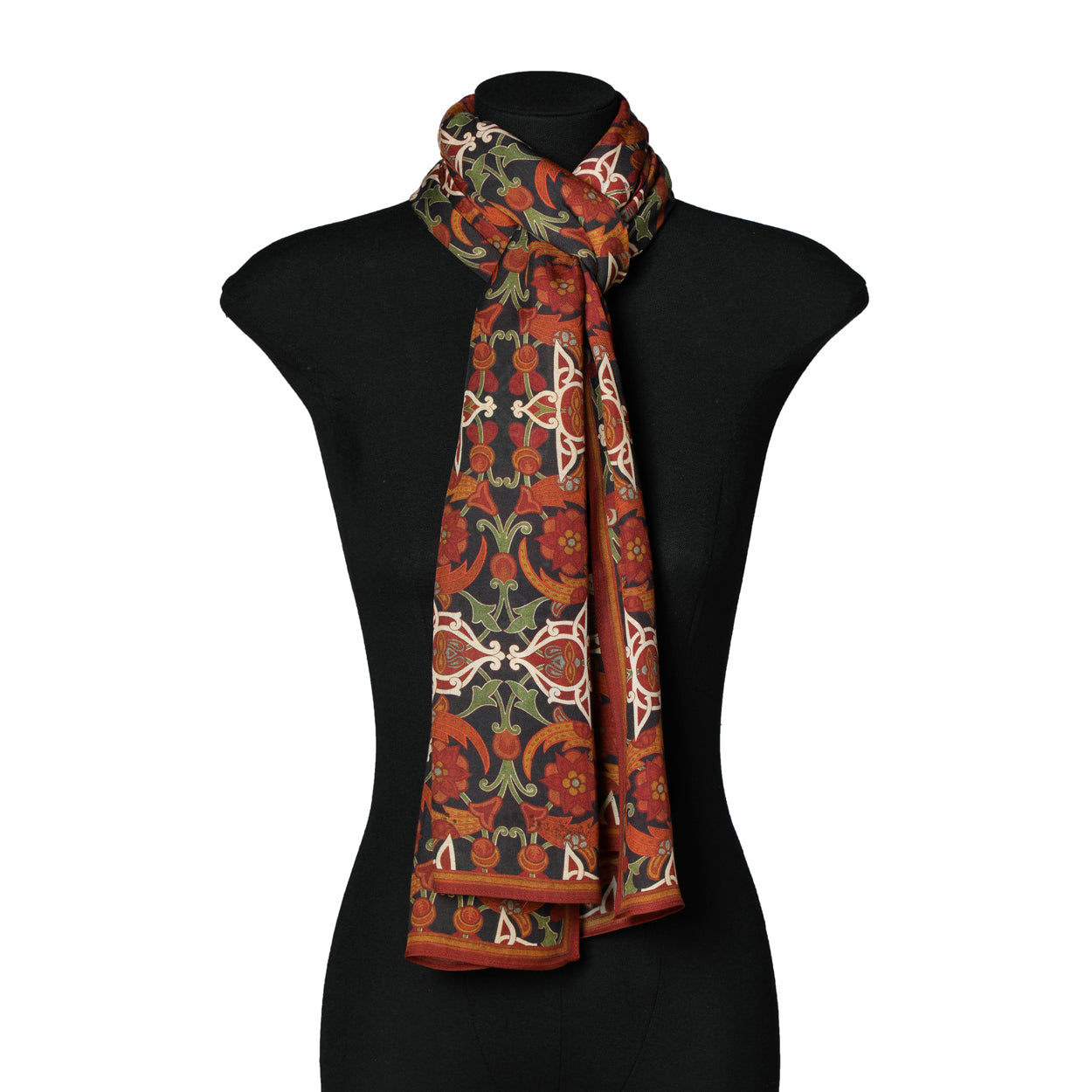 A black mannequin displays the Elegant Womens Scarf with Islamic Art-Inspired Print Samani, a long premium modal accessory with an intricate red, orange, green, and cream floral and geometric design draped stylishly around the neck.