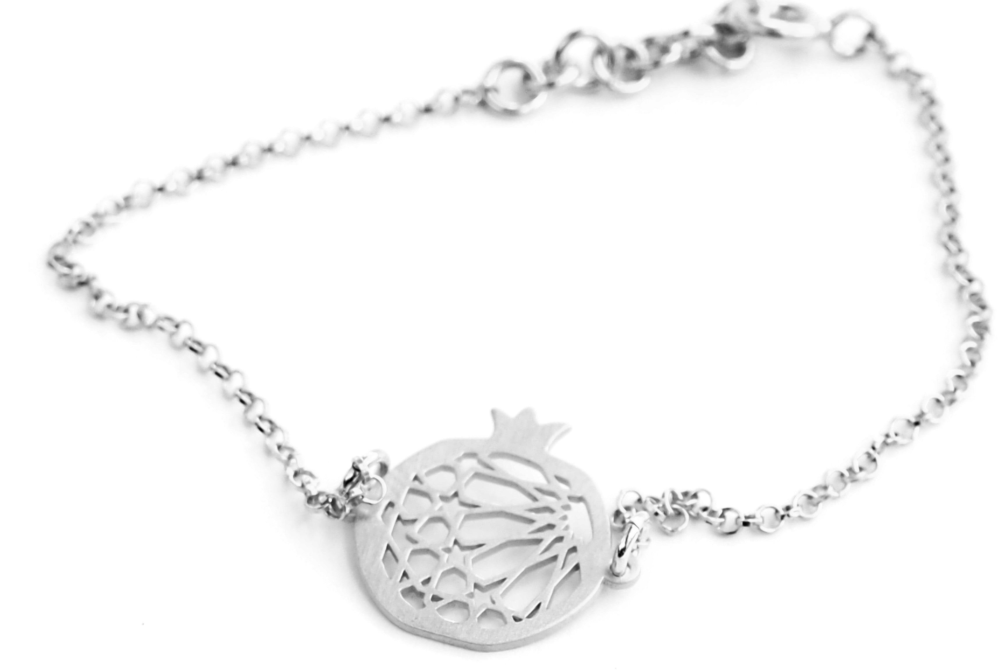The Pomegranate Bracelet No.1 by Platónica is a sterling silver delicate chain bracelet with a stylized pomegranate pendant inspired by Granada, featuring cut-out details and small loops attaching the pendant to the chain.
