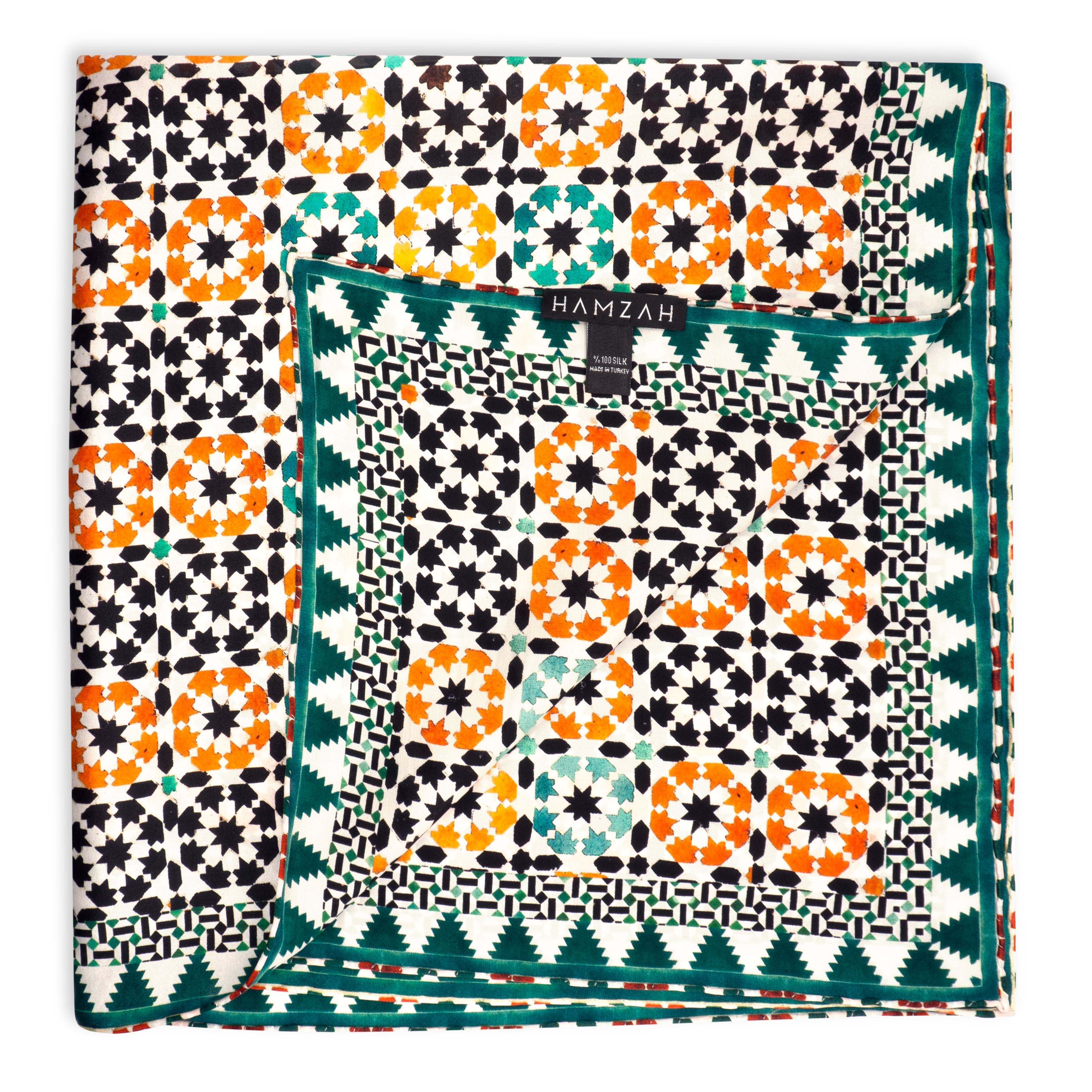 The Islamic Art Square Silk Scarf Sabika Green features intricate geometric patterns in orange, black, white, and green, a decorative border, hand-rolled edges, and a HAMZAH label at the center.