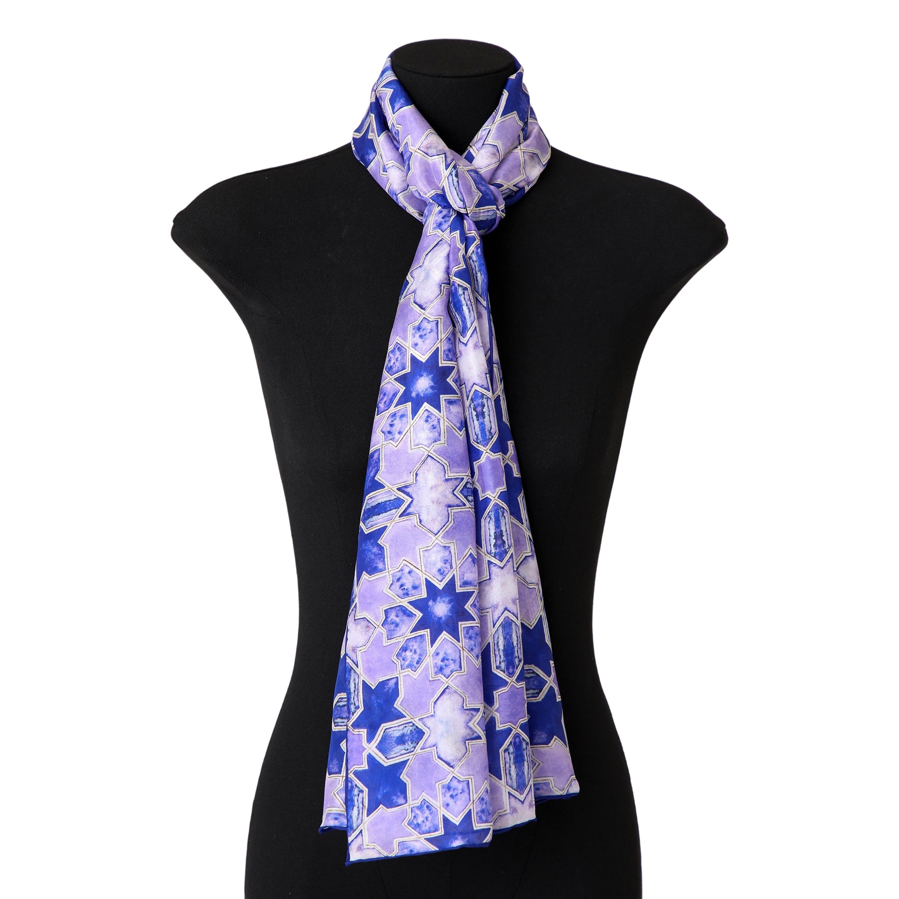 The Purple Silk Scarf with Islamic Art Print Sevilla, featuring a blue and lavender geometric star pattern inspired by Andalusian art, is draped around the neck of a black mannequin torso.