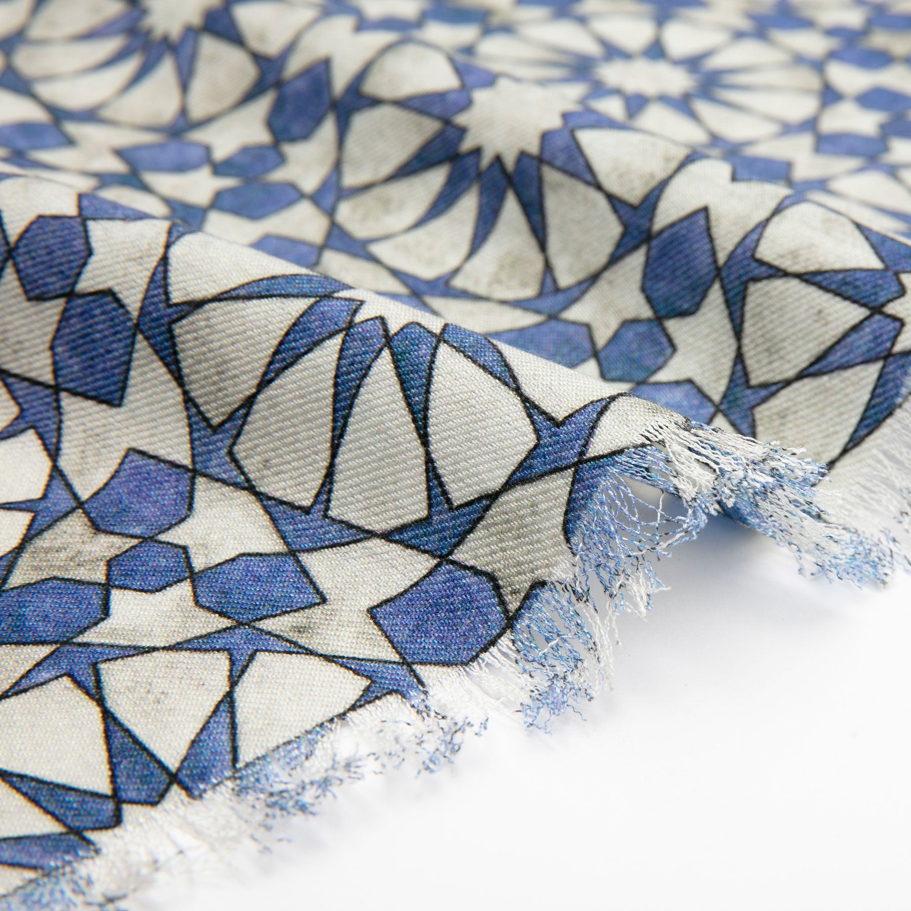A close-up of the Silk and Wool Scarf with Blue and Gray Print highlights its frayed edges, featuring a geometric pattern with repeating star-like shapes that showcase refined cultural artistry.
