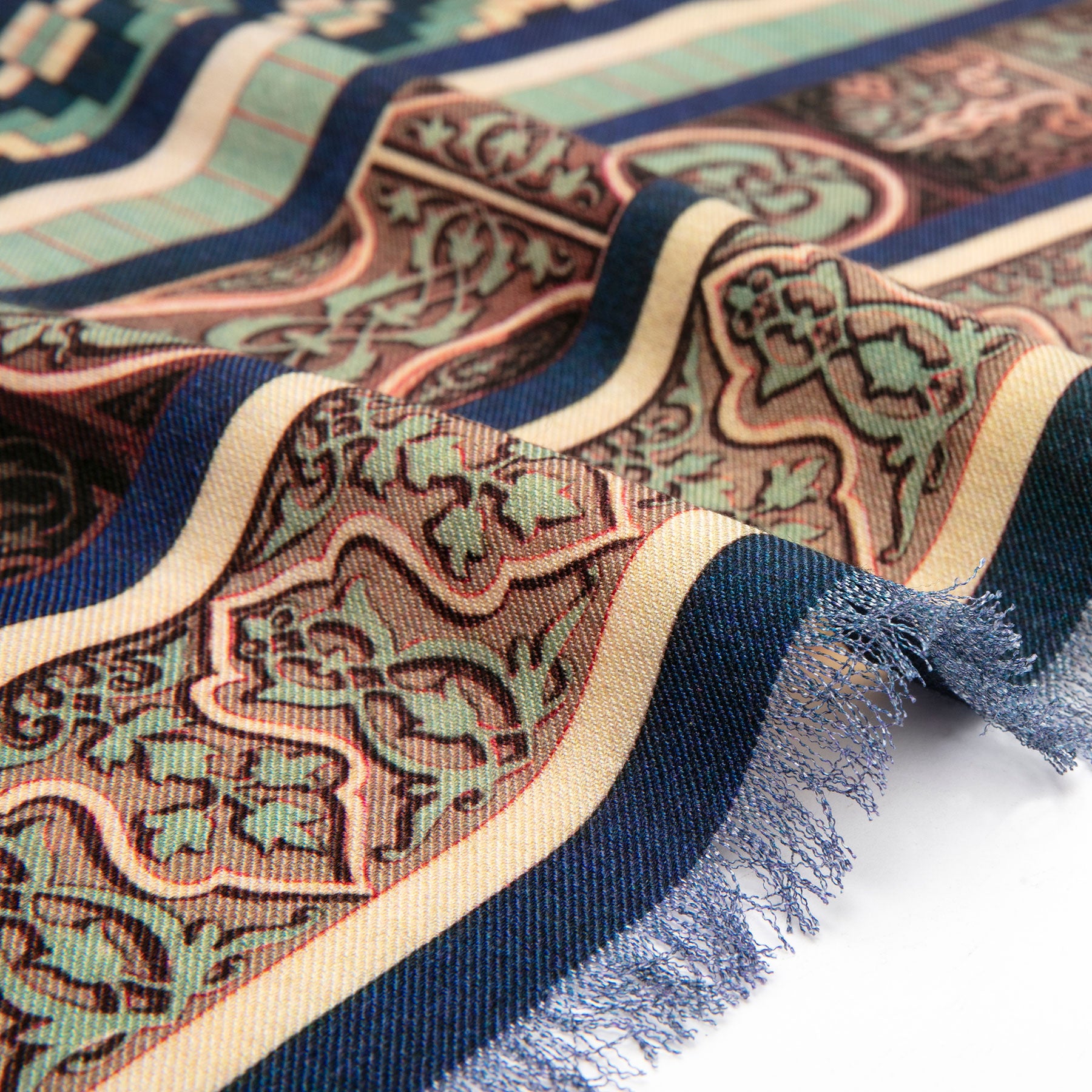 A close-up of the Silk and Wool Scarf Ziyarat, featuring intricate blue, beige, green, and rust designs. Softly folded with frayed edges, the scarf highlights its unique texture and cultural artistry.