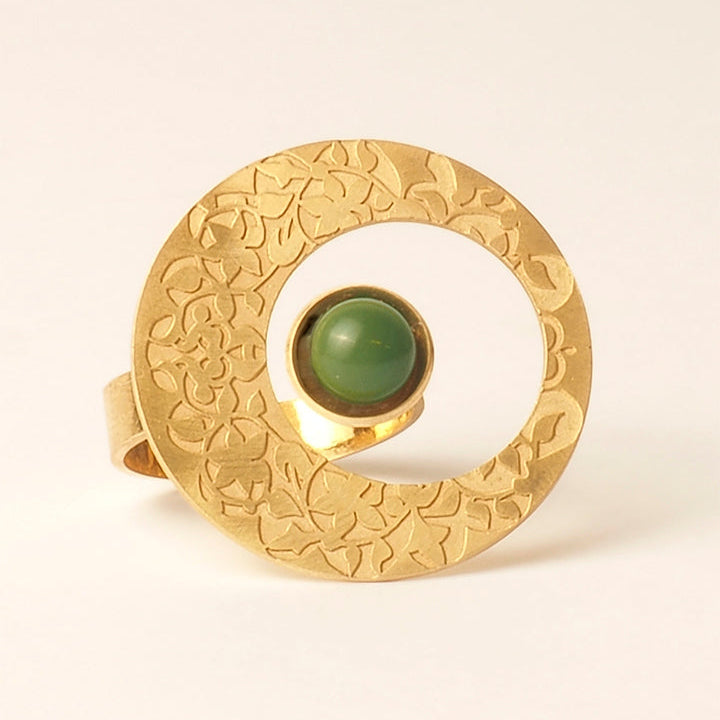 The Platónica Elegant Gold Ring with Alhambra Palace design features a wide, floral-engraved band, an open circular shape, and an off-center striking green glass stone.