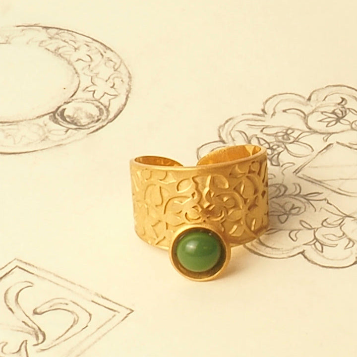The Ring Inspired by Nasrid Motifs Gold & Green from Platónica rests on paper featuring hand-drawn jewelry sketches, including similar adjustable ring designs and motifs inspired by the Alhambra monument.