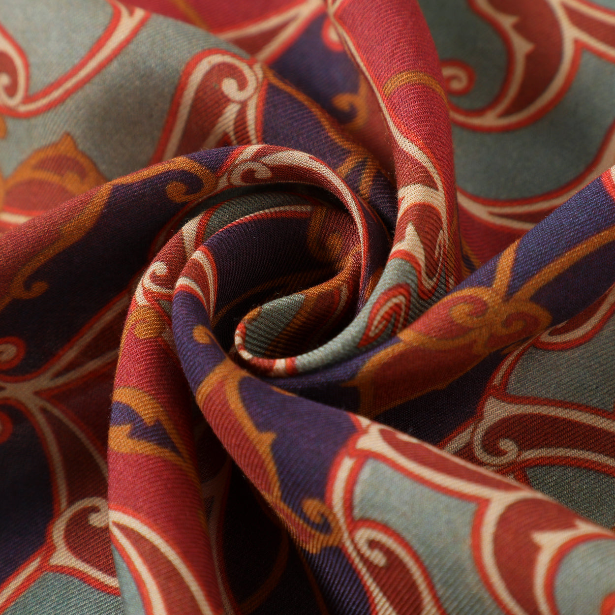 A close-up of the Bukhara-Inspired Scarf Nasafi, showcasing its smooth modal fabric twisted into a spiral to reveal vibrant red, blue, orange, and beige digital prints with intricate Bukhara art motifs.