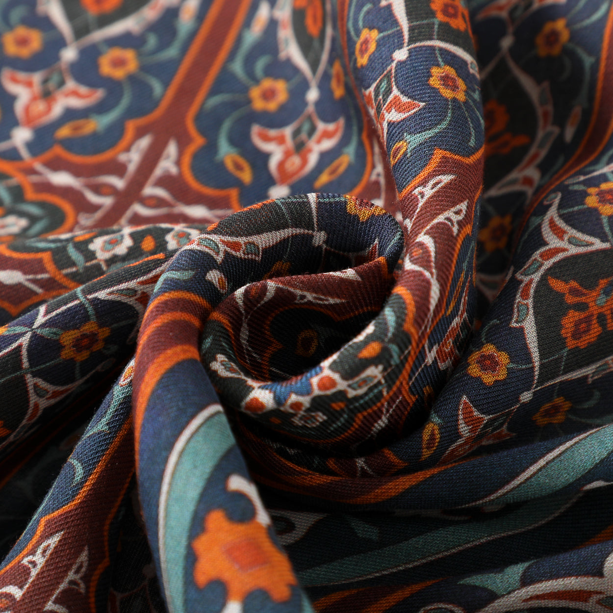 A close-up of the Zarashfan Isfahan-Inspired Scarf, crafted from 100% modal and showcasing intricate Islamic floral designs in blue, rust, orange, and green, softly folded into a spiral shape.