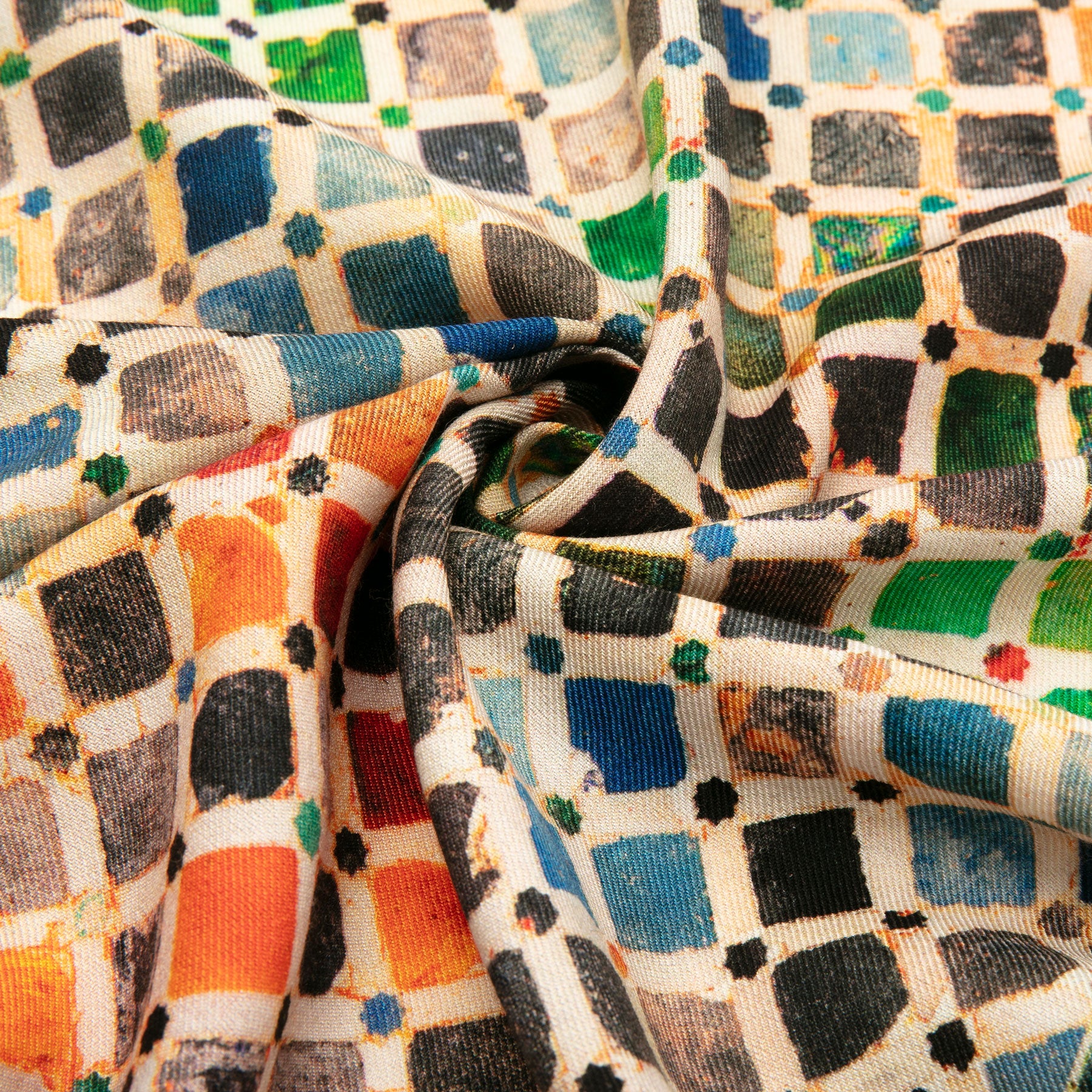 Close-up of the Silk Wool Scarf Comares, showcasing its vibrant geometric pattern with blue, green, orange, and black squares. The twisted center highlights the scarfs folds, texture, and cultural artistry.